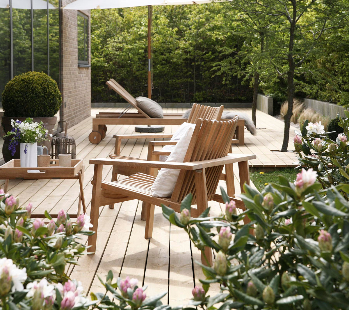 Sillas de madera y una mesa están rodeadas de vegetación y flores, creando un área de asientos al aire libre serena y acogedora.