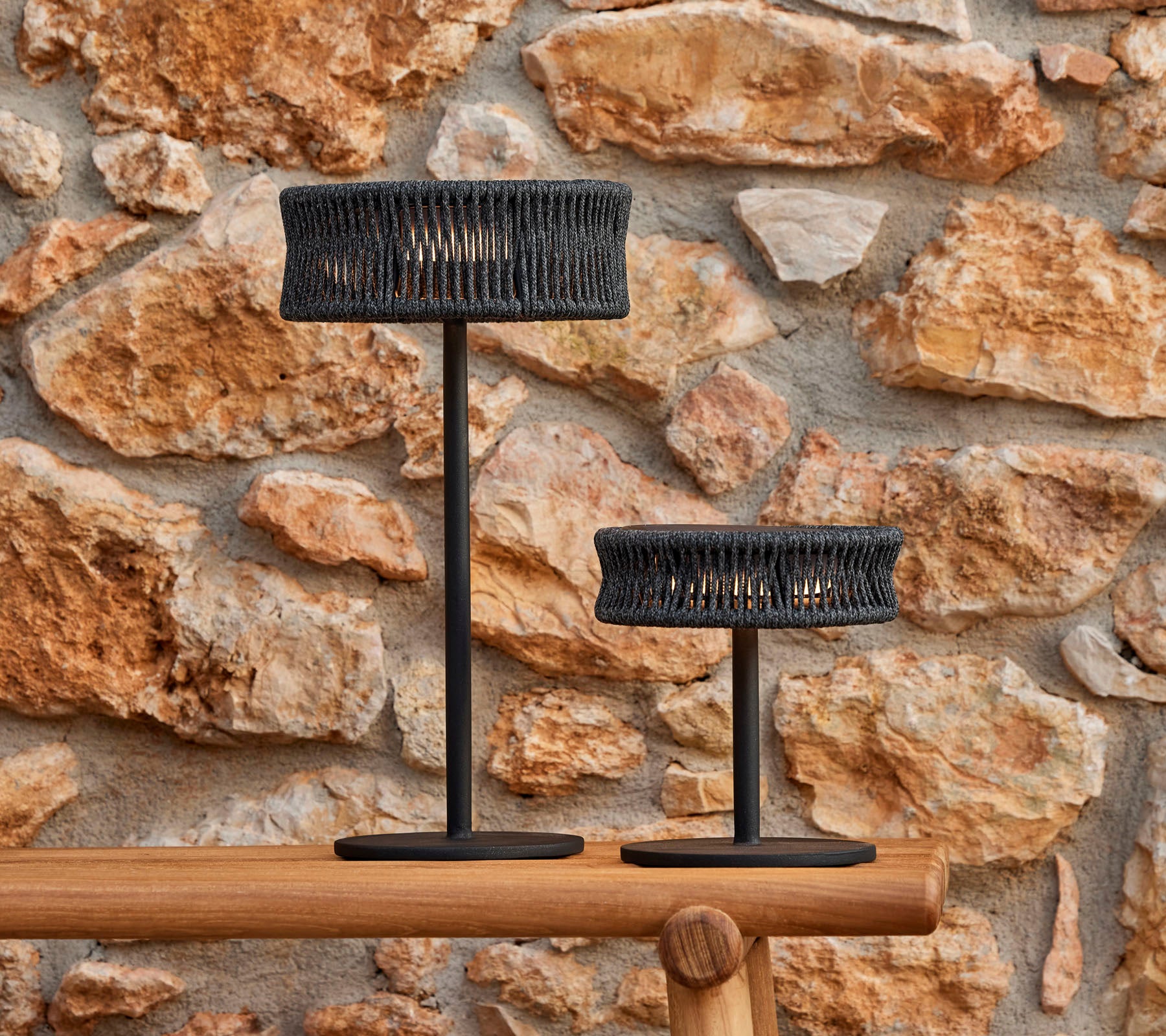 Dos lámparas de mesa elegantes con un diseño trenzado, contra una pared de piedra texturizada, creando una atmósfera elegante y acogedora.