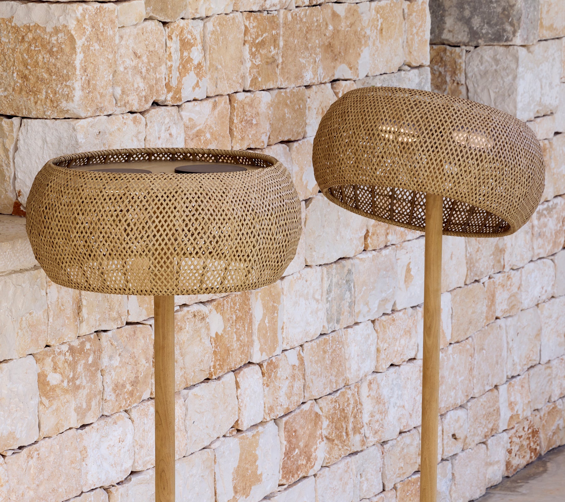 Dos pantallas de lámparas tejidas en lámparas de pie contra una pared de piedra.