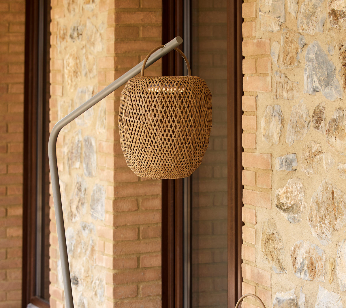 Una lámpara tejida y luminosa suspendida de un soporte elegante, que complementa una pared de piedra texturizada.