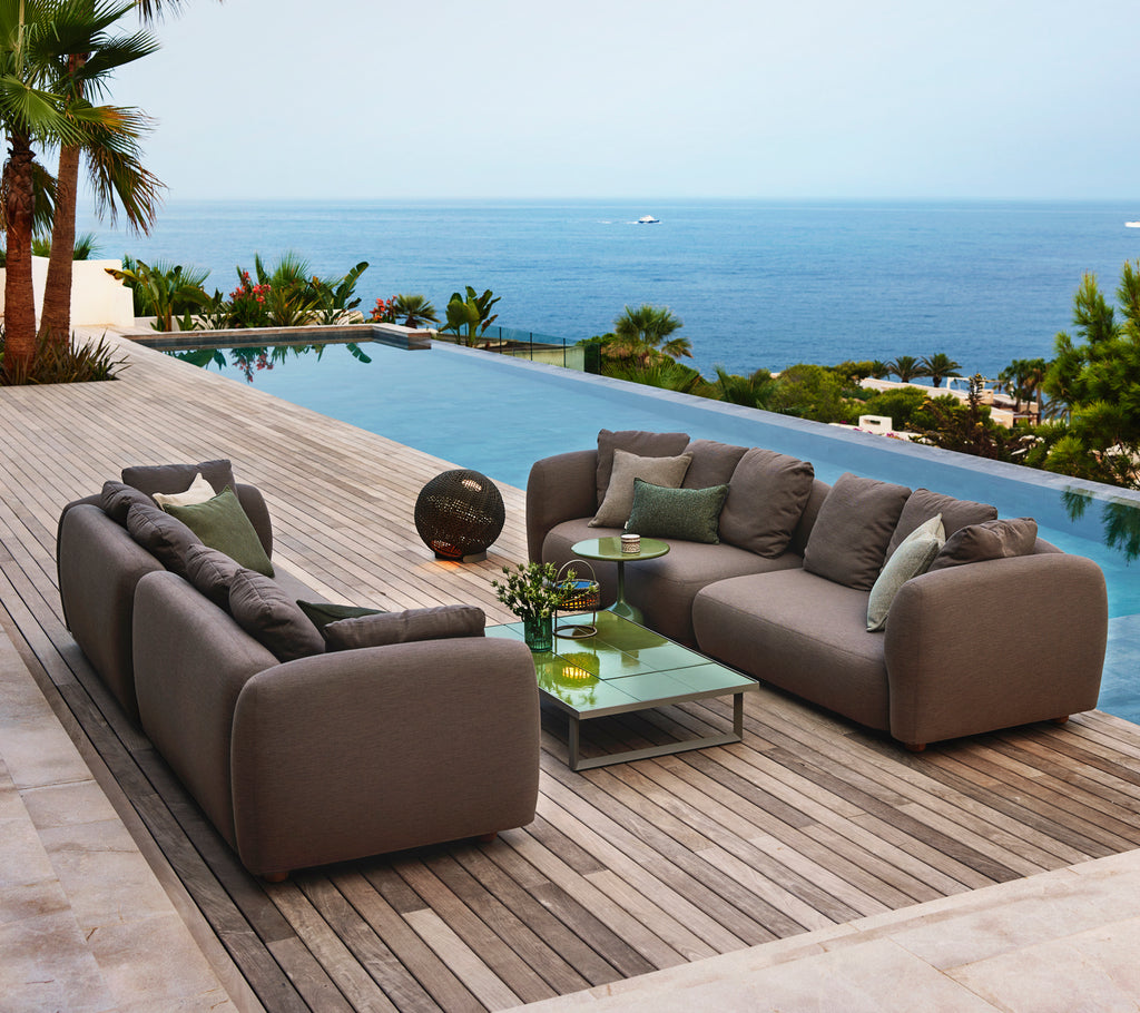 Asientos de salón elegantes con suaves cojines grises, una mesa de café de vidrio y una serena vista al océano. Ideal para relajarse.