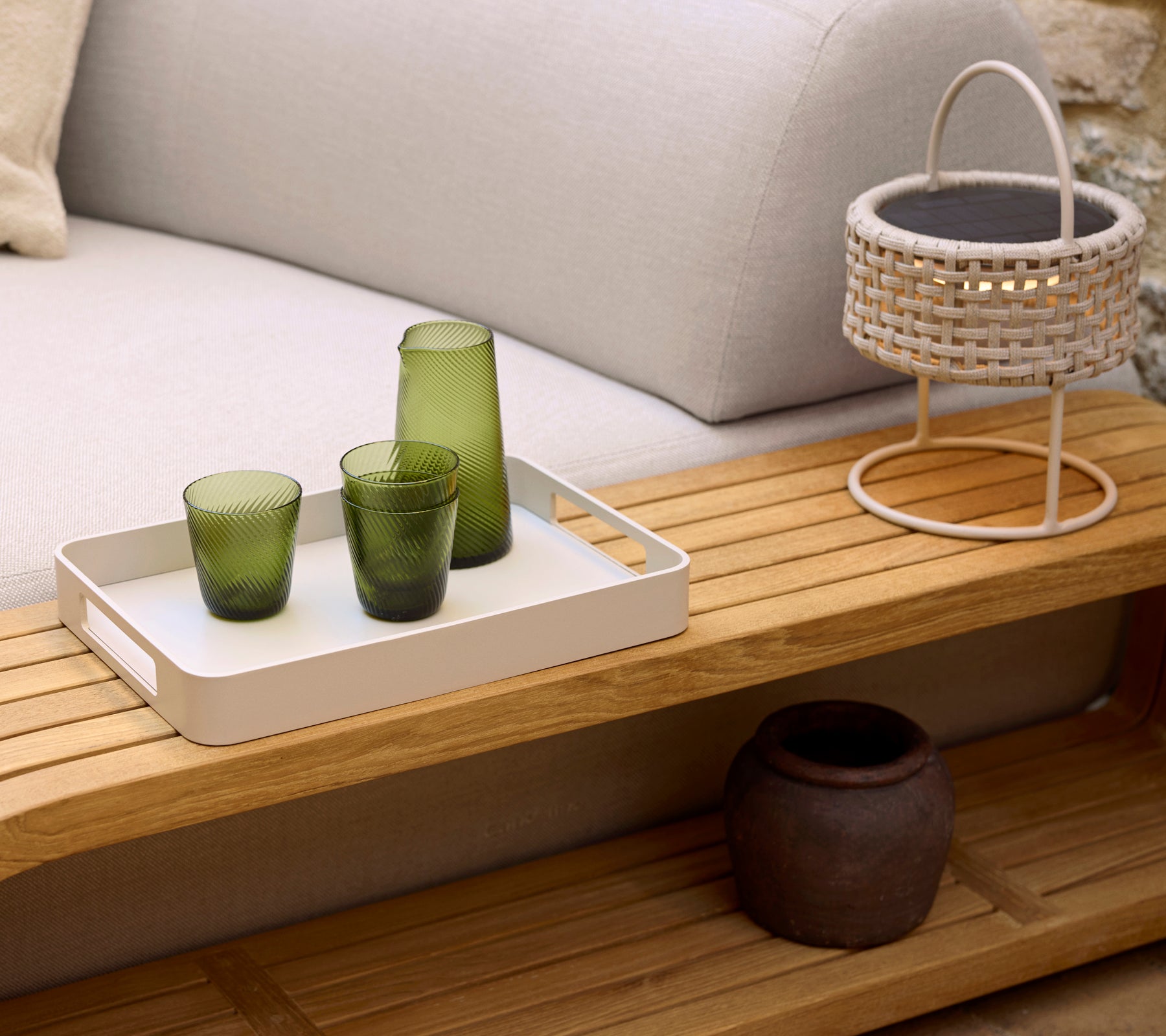 Una mesa de café acogedora con una bandeja blanca, tres vasos verdes, una lámpara tejida y una maceta decorativa, que realza una atmósfera serena.