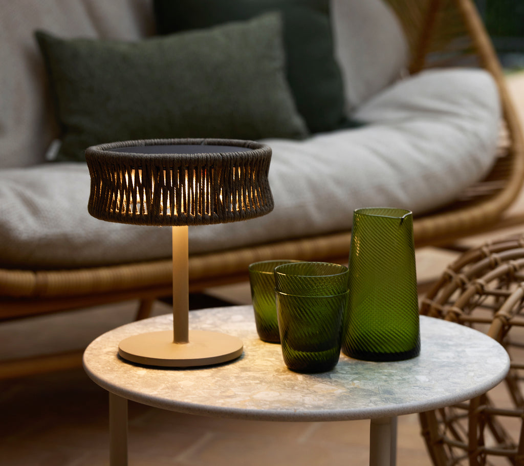 Una pequeña lámpara de ilusión gris oscuro sobre una mesa de café de mármol, acompañada de jarrones de cristal decorativos verdes y un área de asientos acogedora.