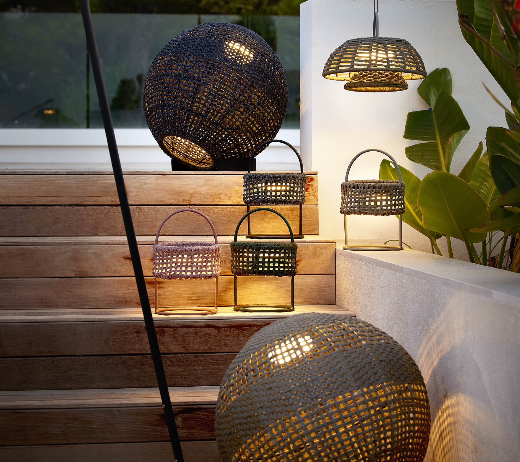 Una colección de lámparas de ilusión elegantes en varias formas, que emiten una cálida y acogedora luz entre la vegetación decorativa.