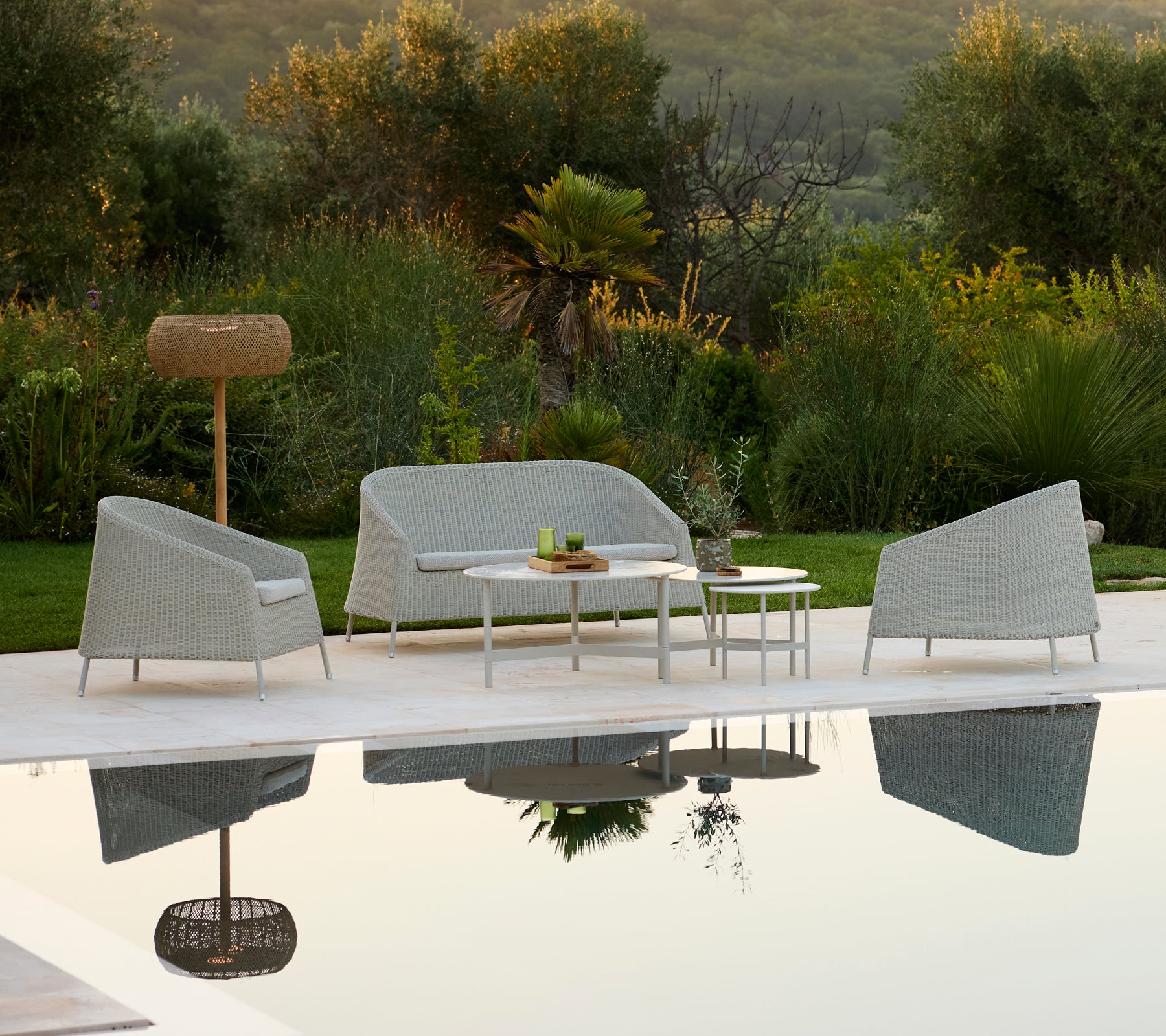 Sofá y silla gris modernos con mesa blanca en un ambiente de lounge al aire libre.