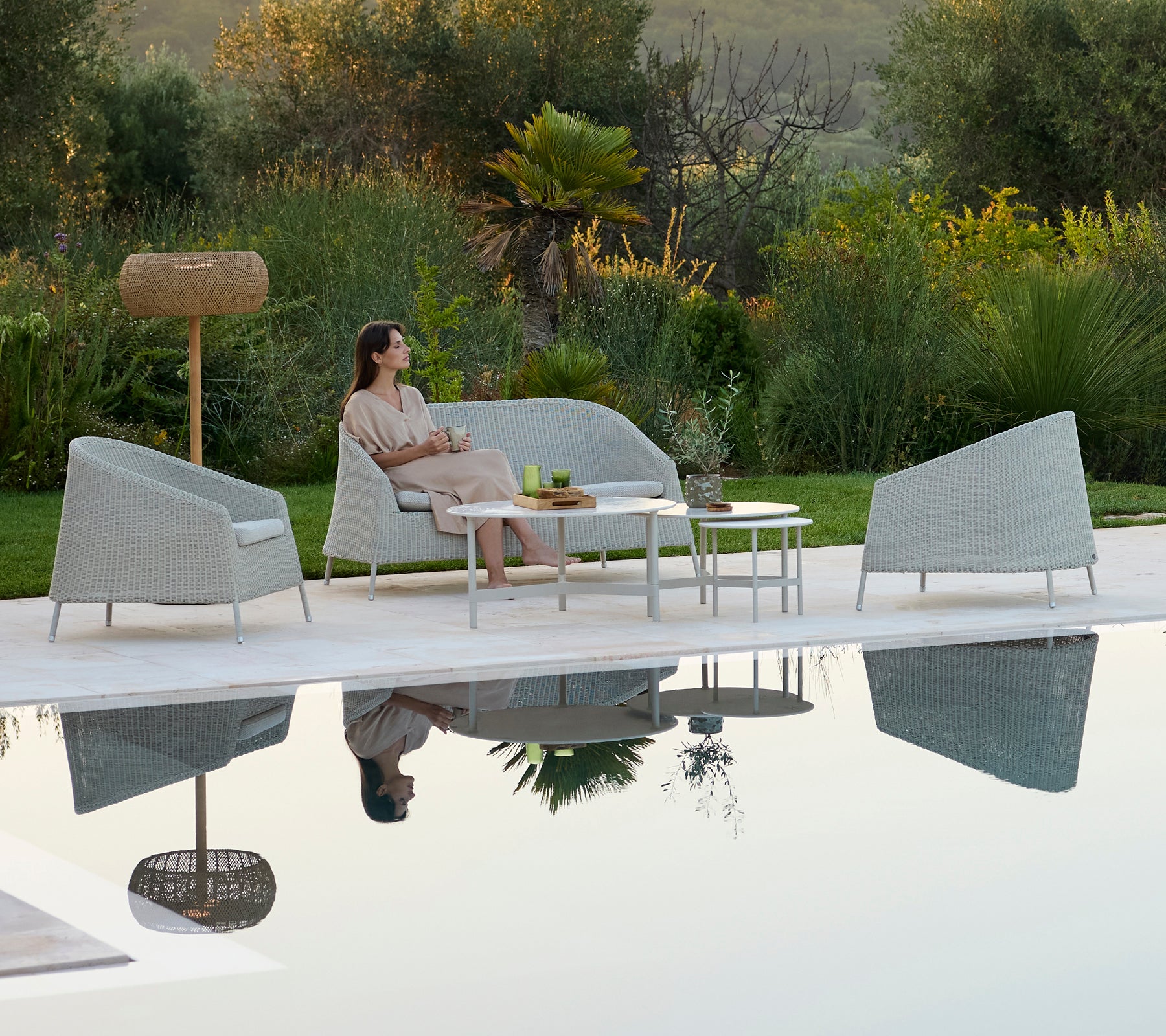 Sofá gris moderno y sillones alrededor de una mesa blanca en una relajante zona de estar al aire libre.