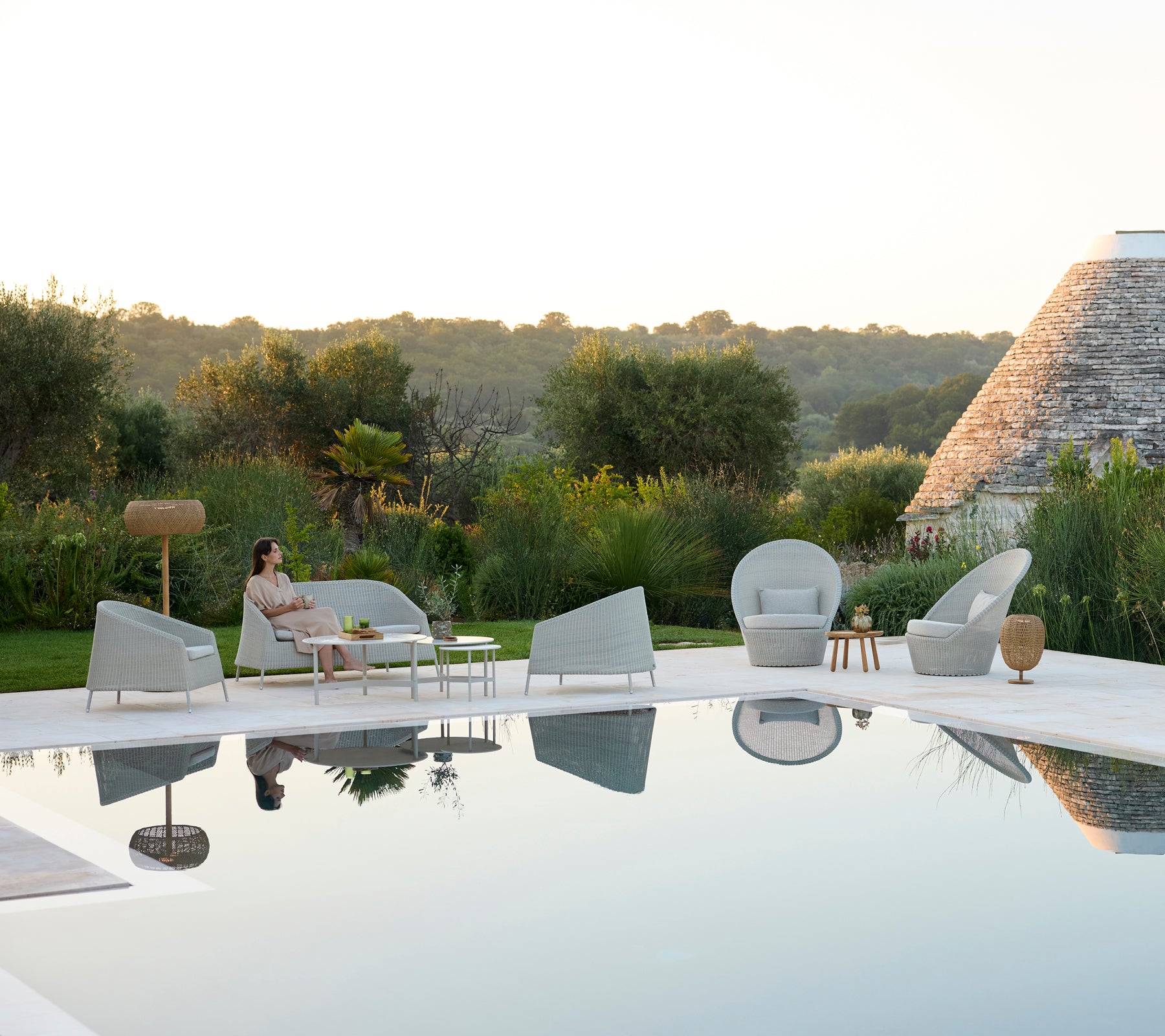 Moderno área de salón al aire libre con sillas grises y una mesa blanca junto a una piscina.