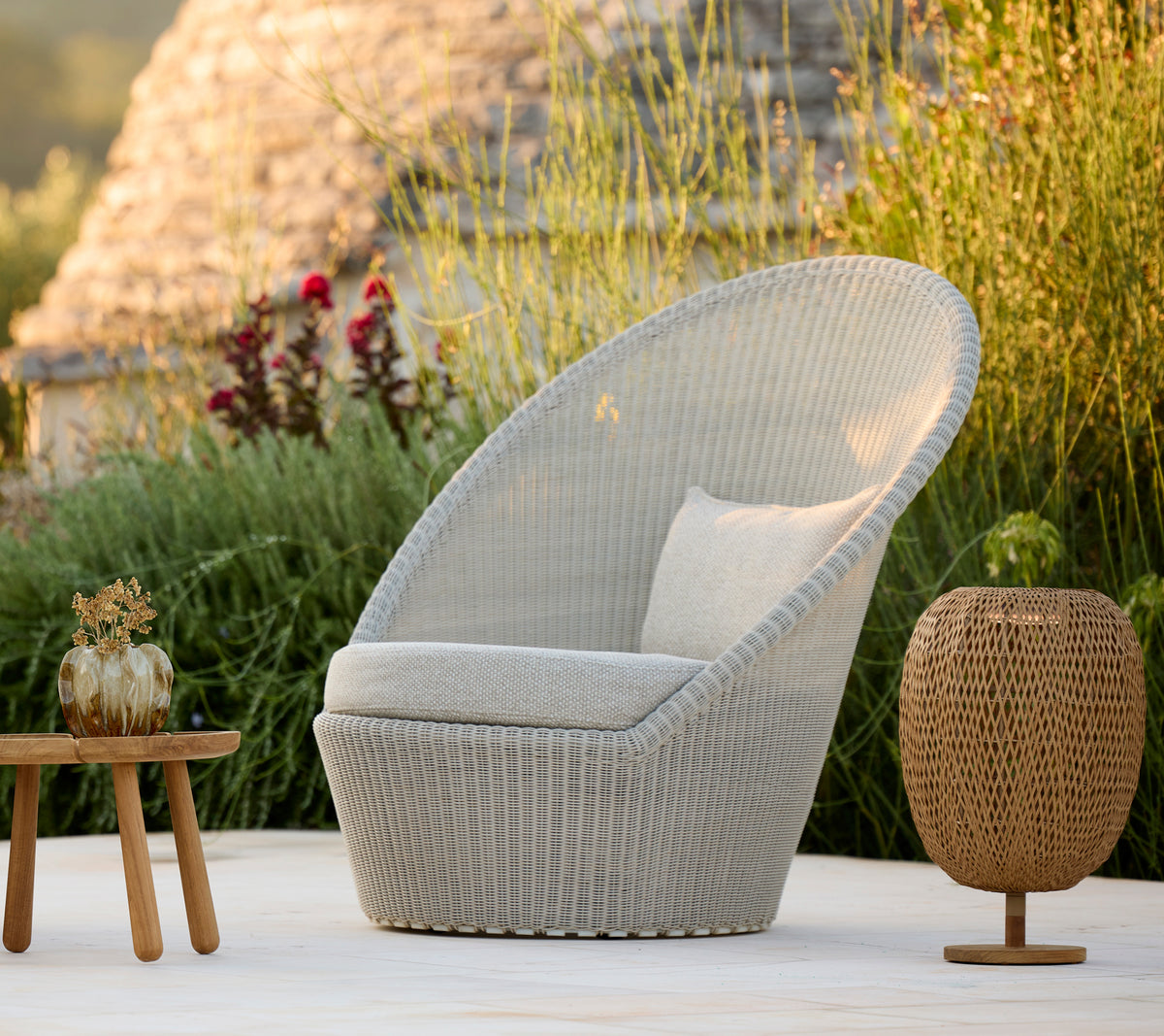 Silla moderna gris con cojín y mesa marrón en un entorno natural al aire libre.