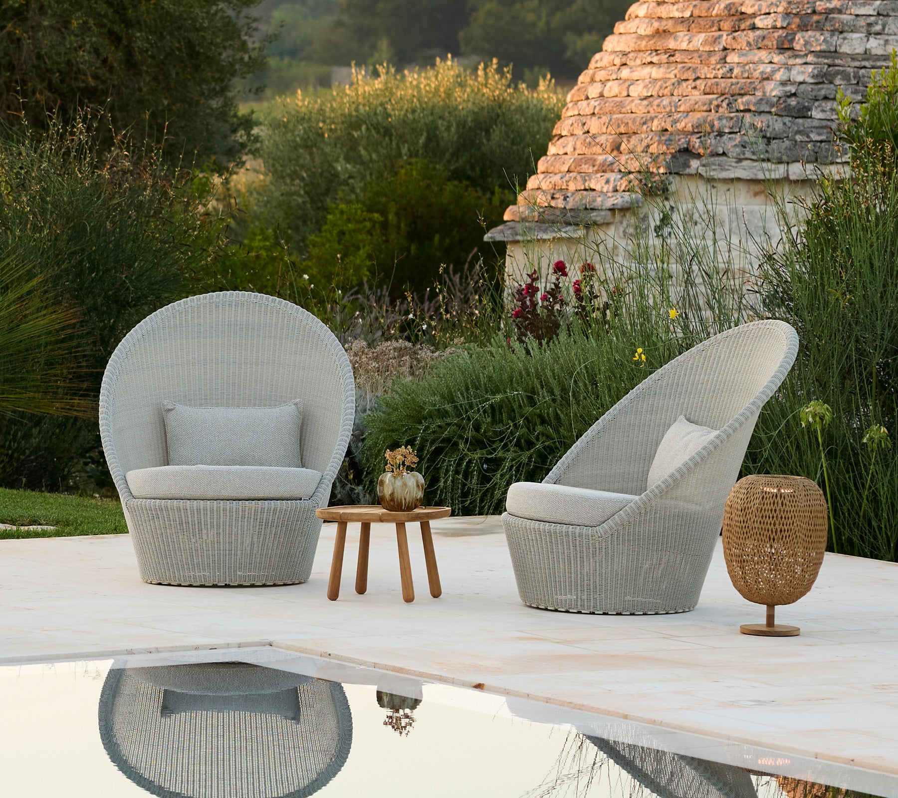 Dos sillones grises y una mesa de madera al lado de una piscina en un entorno exterior moderno.