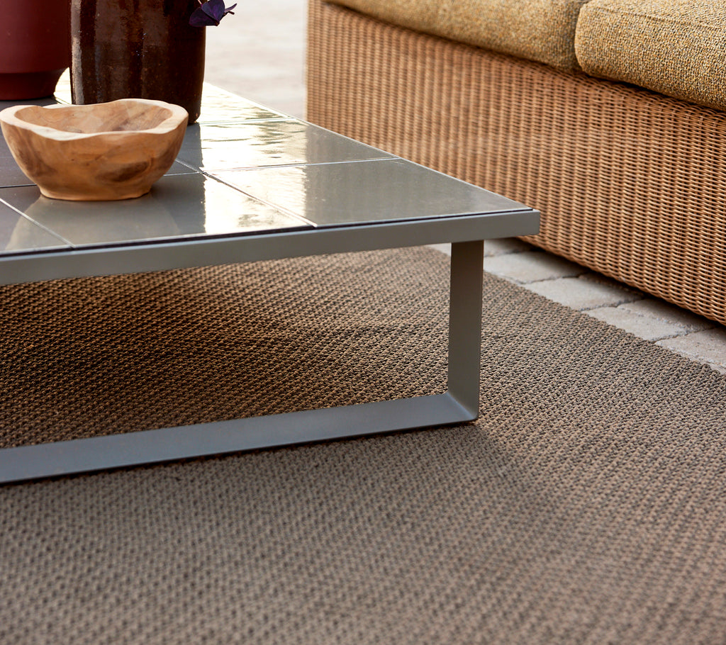 Una alfombra de punto emparejada con una mesa de café vidriada y un tazón de madera encima, creando un ambiente elegante y acogedor.