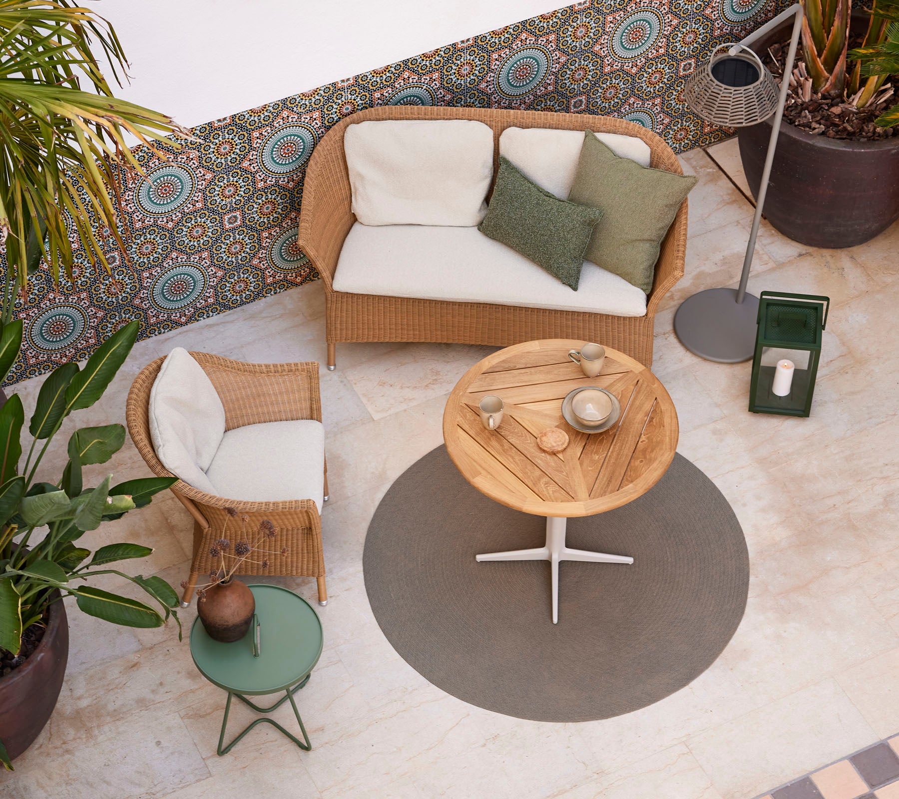 Un acogedor espacio de asiento con un sofá de ratán, una mesa de café de madera redonda y plantas en macetas, que realzan una atmósfera elegante.