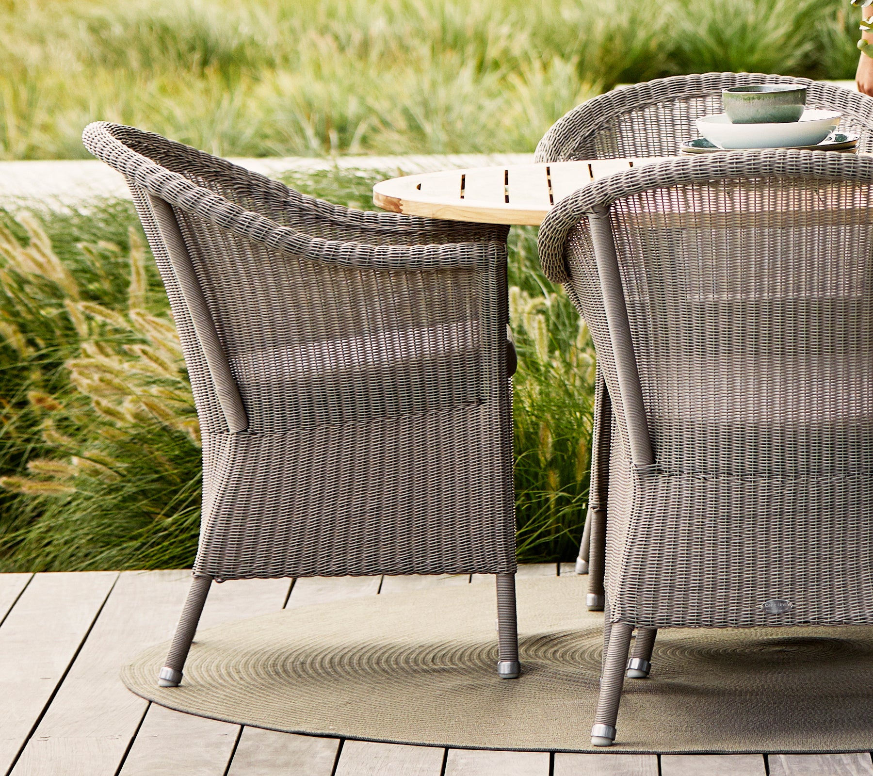Sillas Taupe Lansing con diseño tejido texturizado, combinadas con una mesa de madera natural y rodeadas de exuberante vegetación.