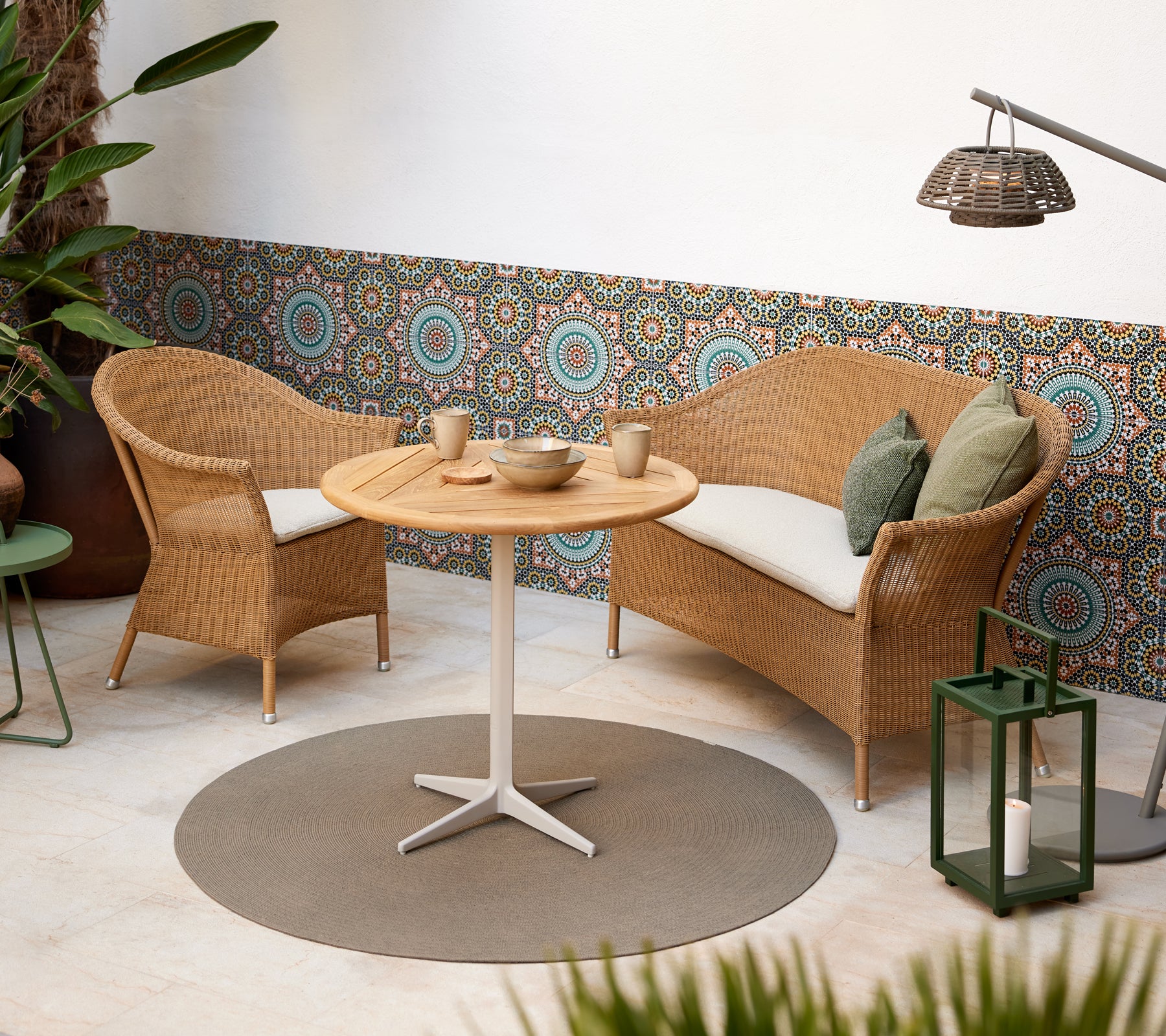 Una acogedora área de estar con sillas de mimbre y una mesa redonda, complementada con vibrantes patrones circulares de fondo.