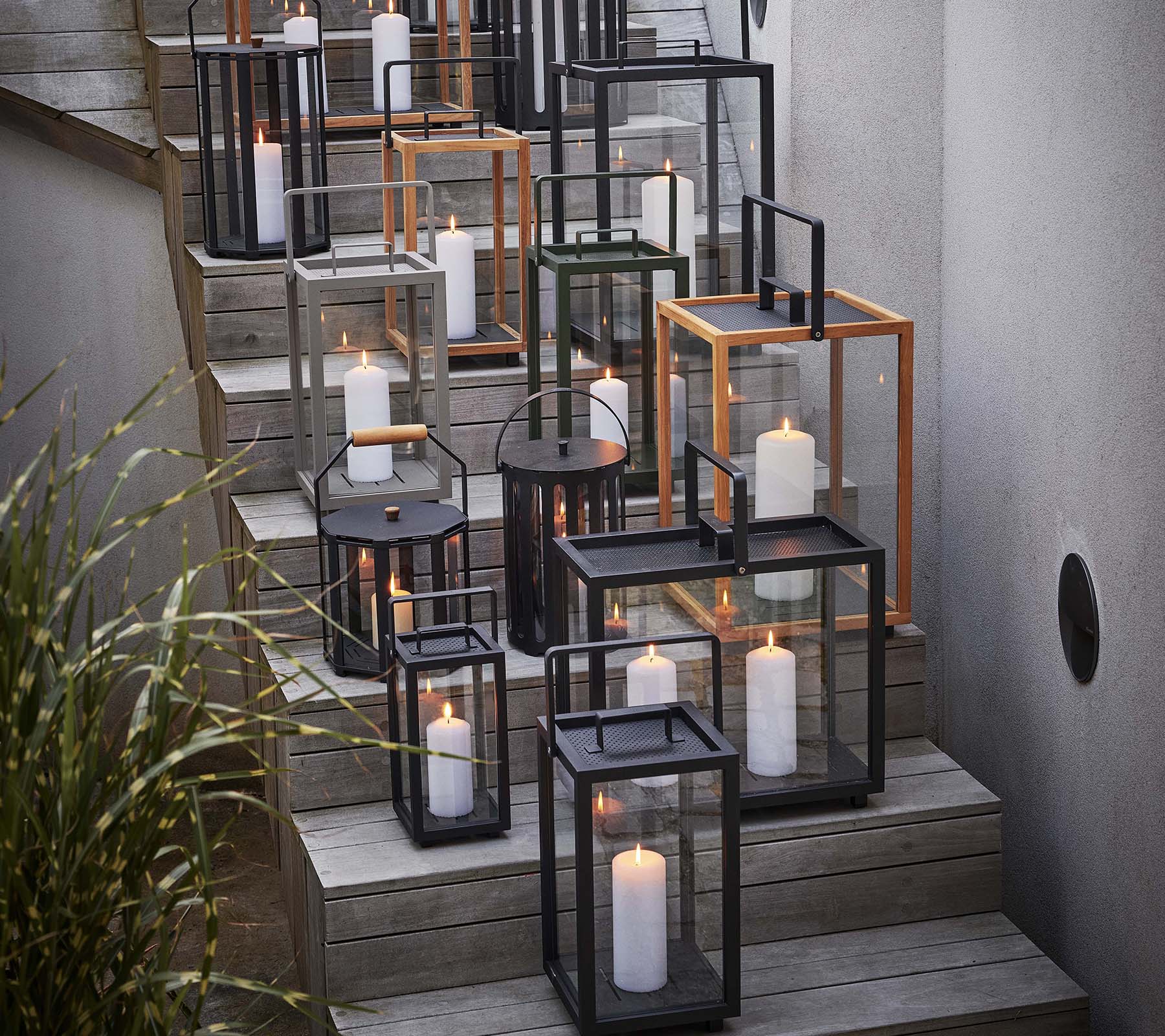 Una colección de varias linternas con velas dispuestas en una escalera, mostrando una mezcla de marcos negros y metálicos.