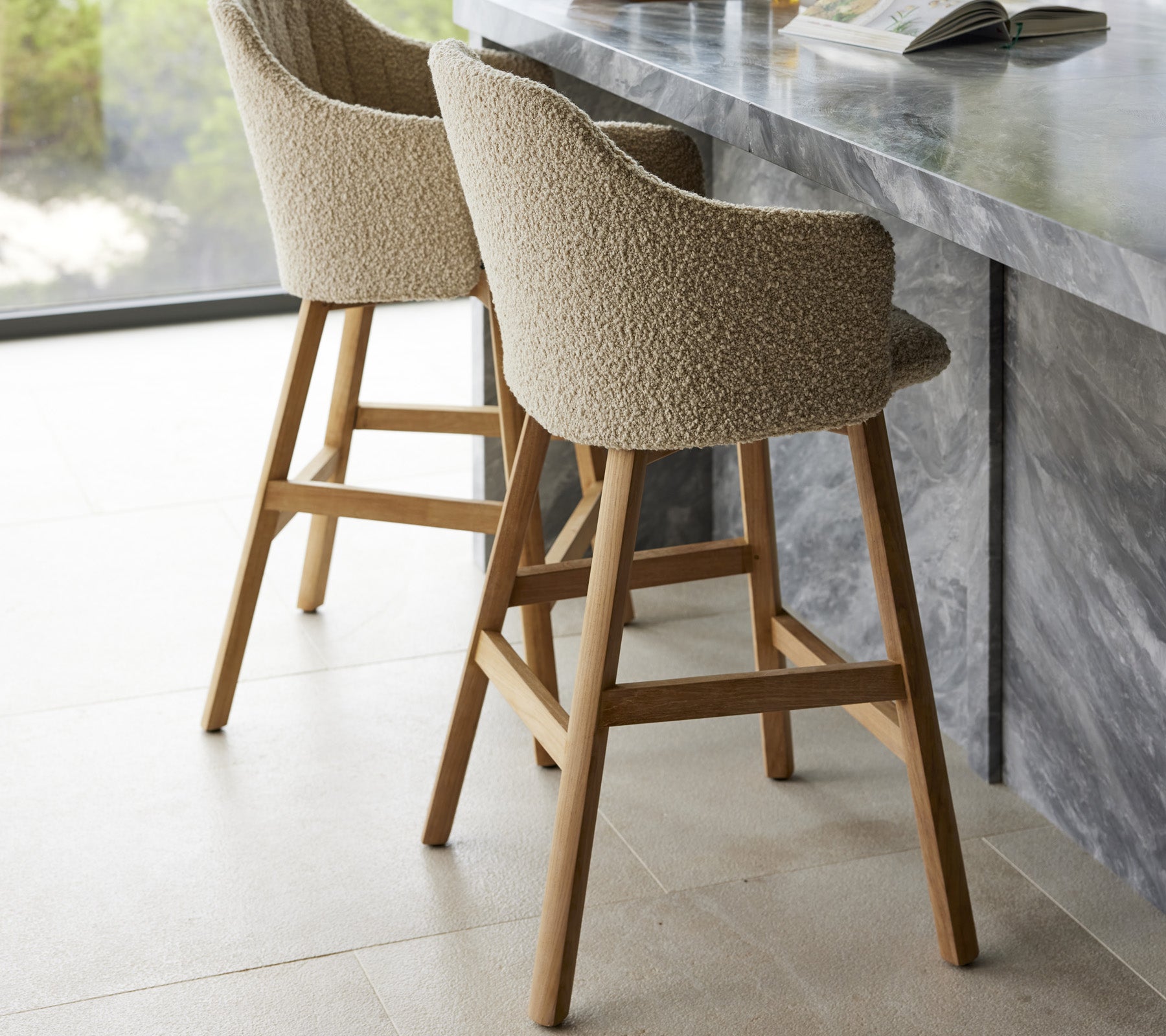 Dos taburetes de bar modernos con asientos acolchados y patas de madera, situados cerca de un elegante mostrador de mármol.