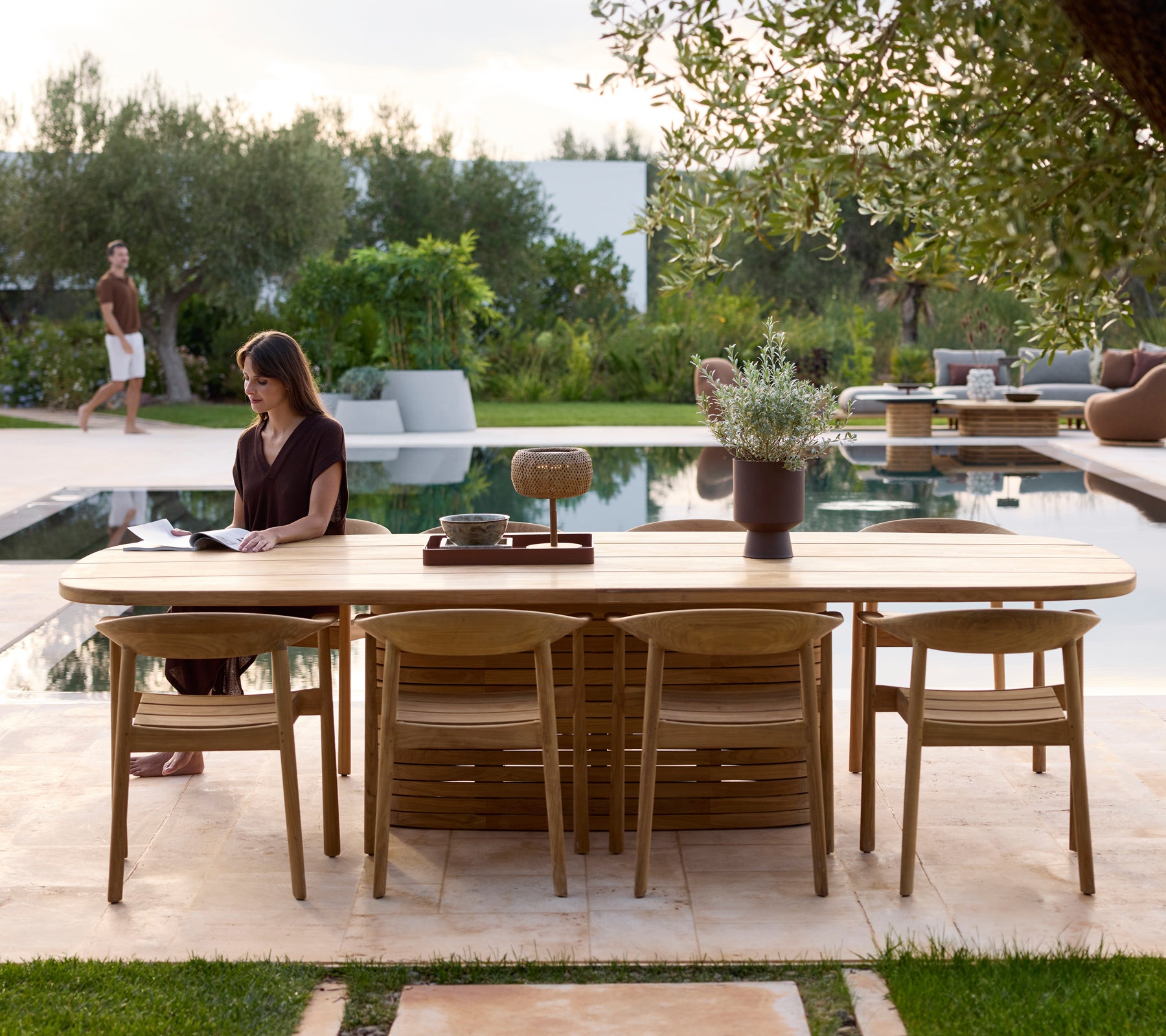 Mesa de exterior moderna con sillas junto a una piscina rodeada de vegetación.