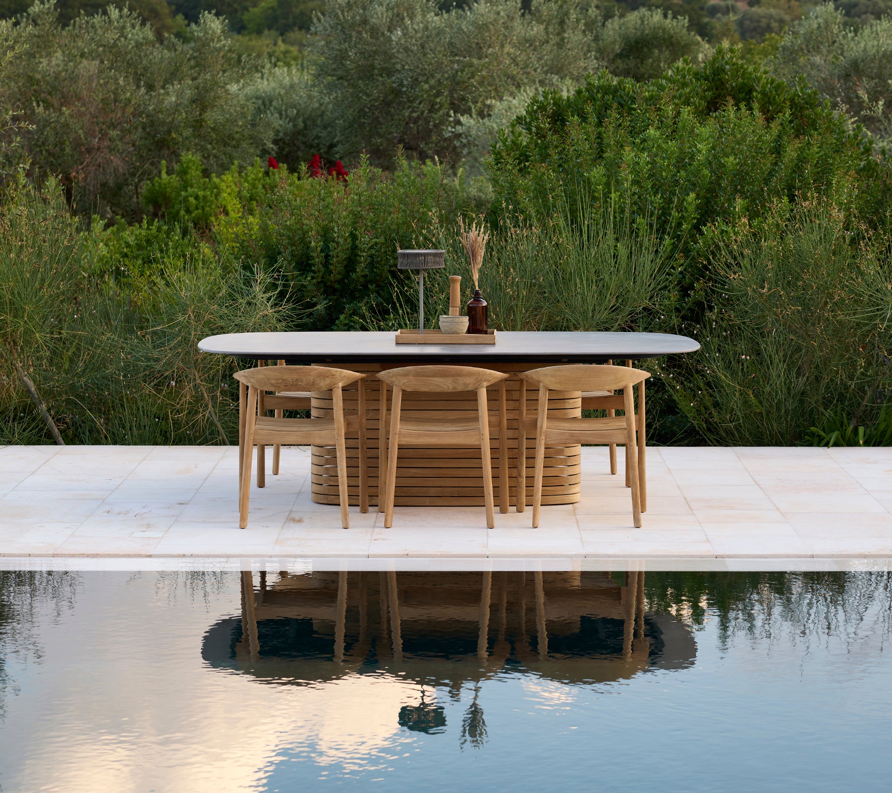 Mesa de exterior moderna con sillas junto a una piscina y rodeada de vegetación.