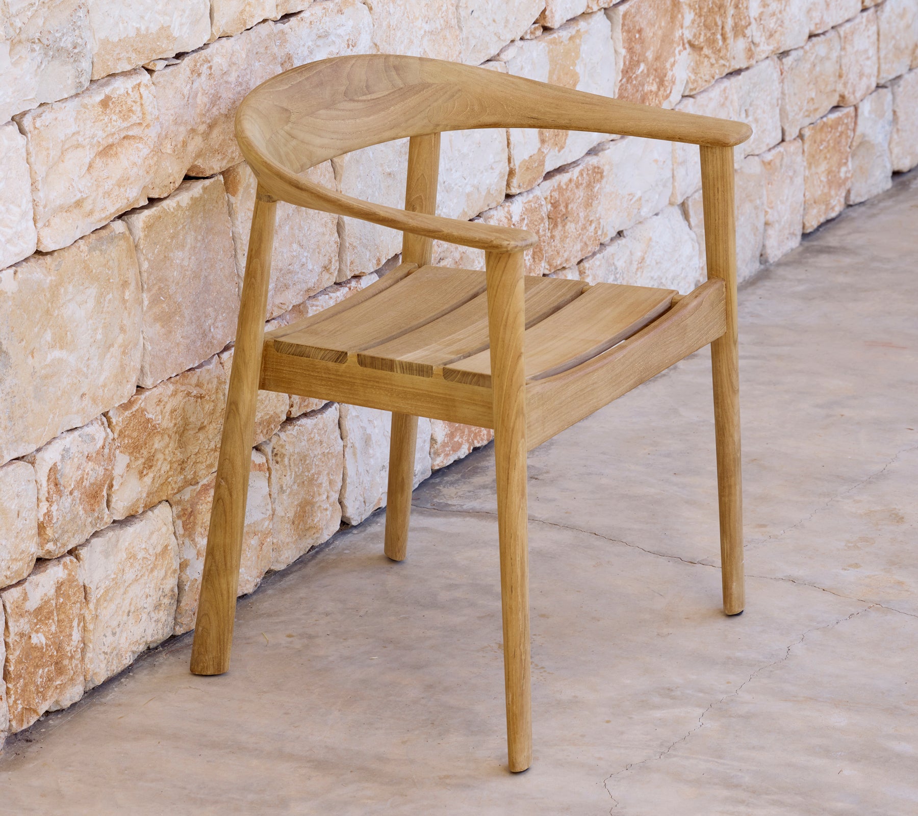 Silla moderna de madera al lado de una pared de piedra en un entorno minimalista.
