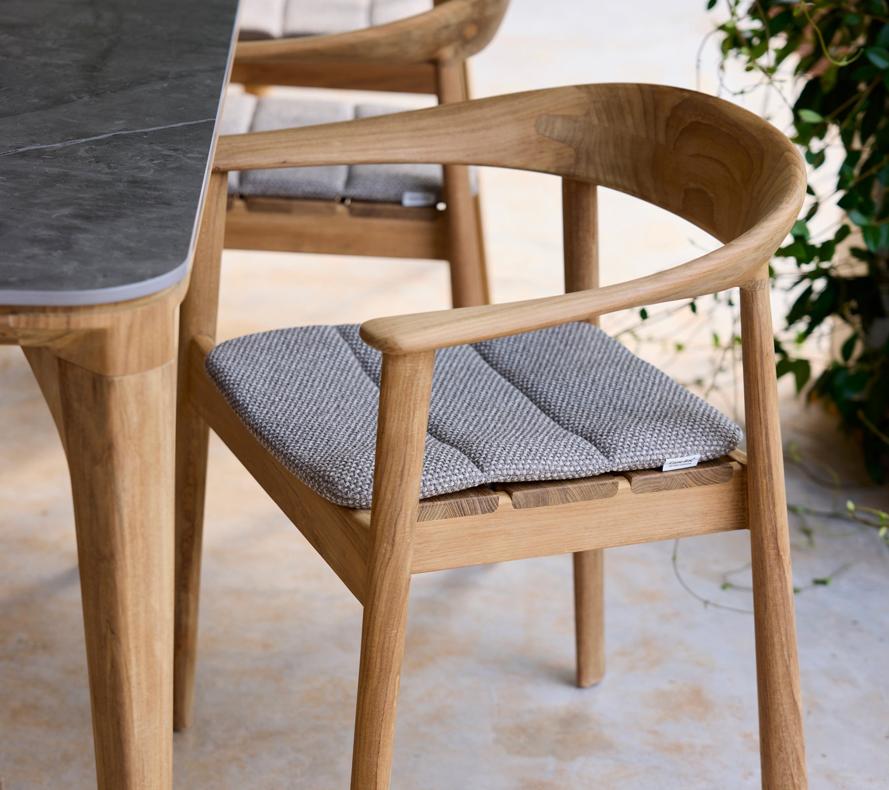 Silla de madera moderna con cojín gris al lado de una mesa en un ambiente de salón.