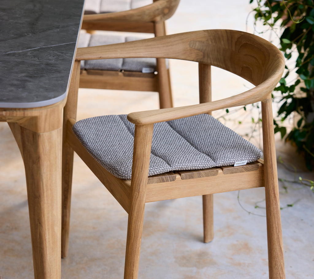 Silla de madera moderna con cojín gris al lado de una mesa en un ambiente de salón.