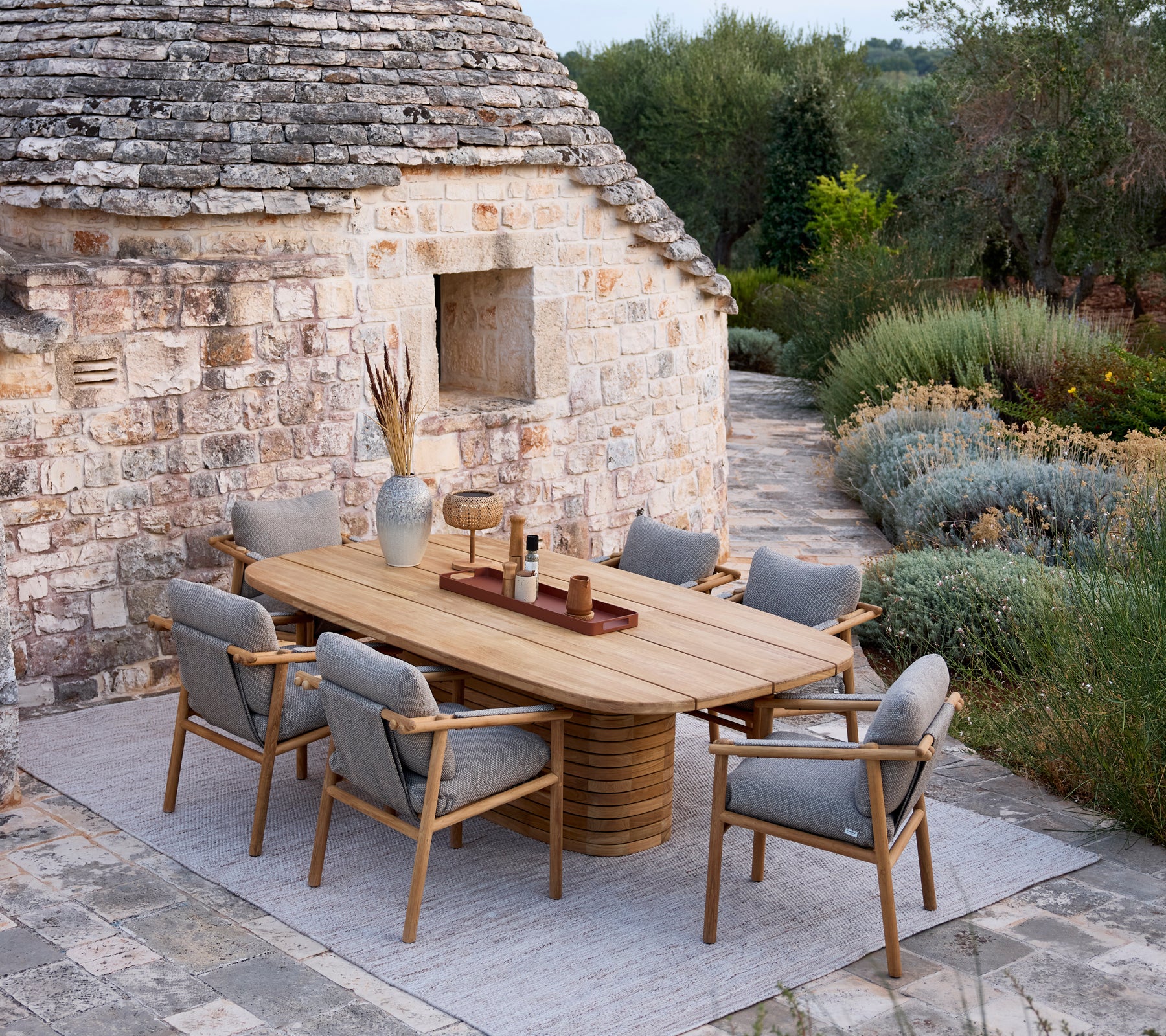 Mesa de comedor de madera con sillas con cojín gris en un entorno rústico al aire libre.