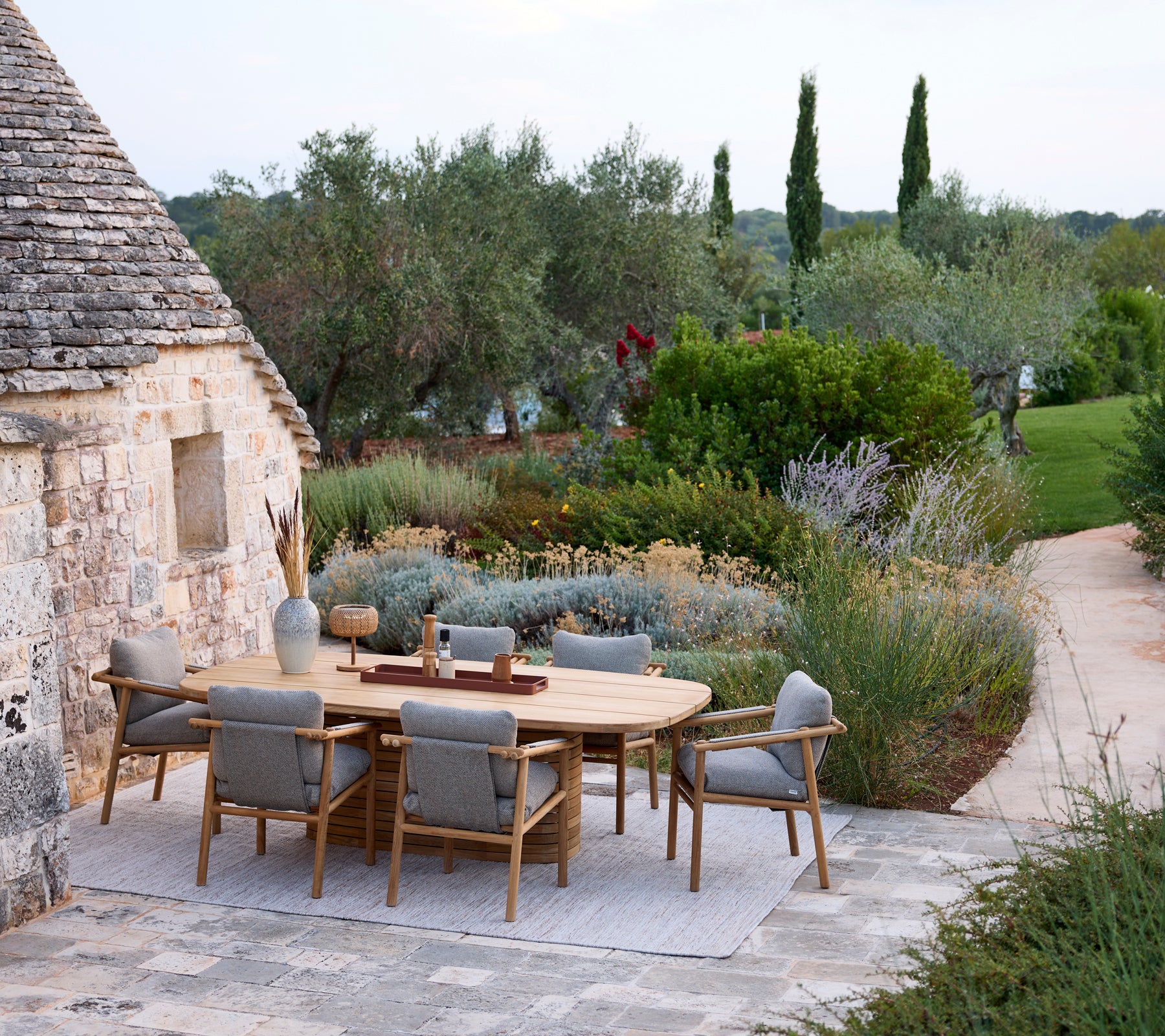 Configuración moderna de comedor al aire libre con una mesa redonda y sillas grises rodeadas de vegetación.