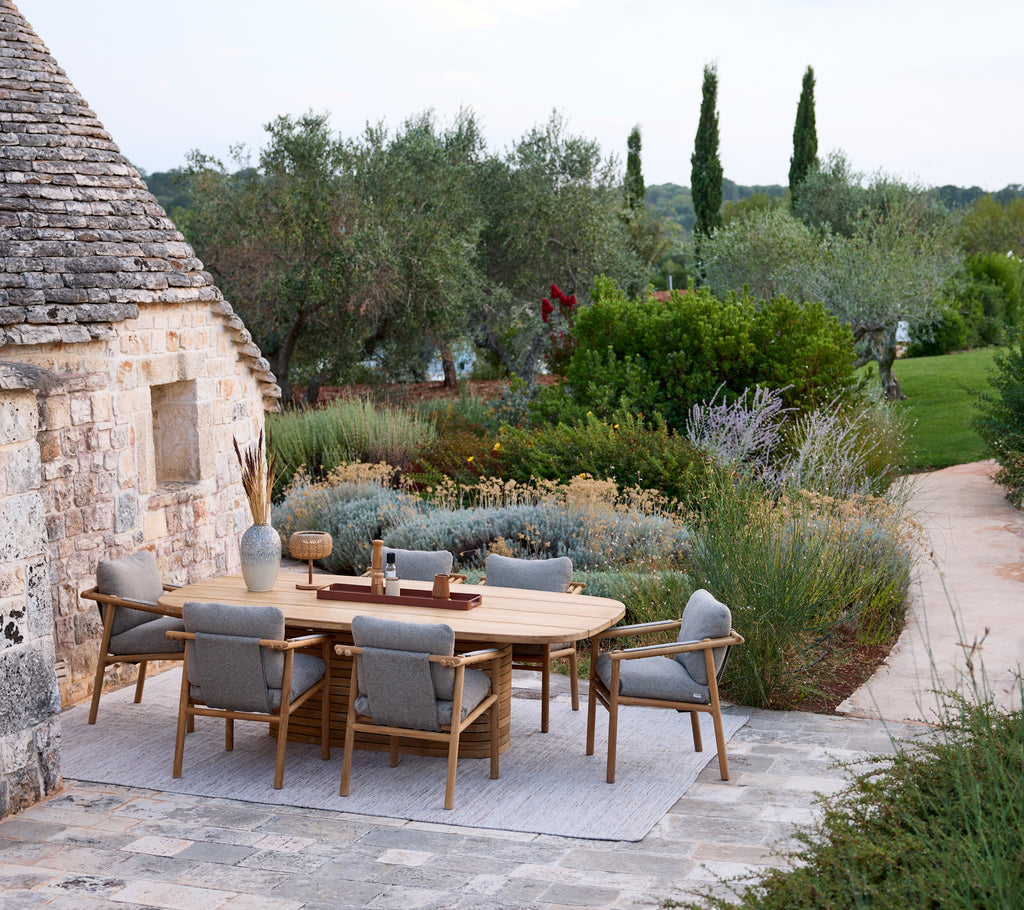 Configuración moderna de comedor al aire libre con una mesa redonda y sillas grises rodeadas de vegetación.