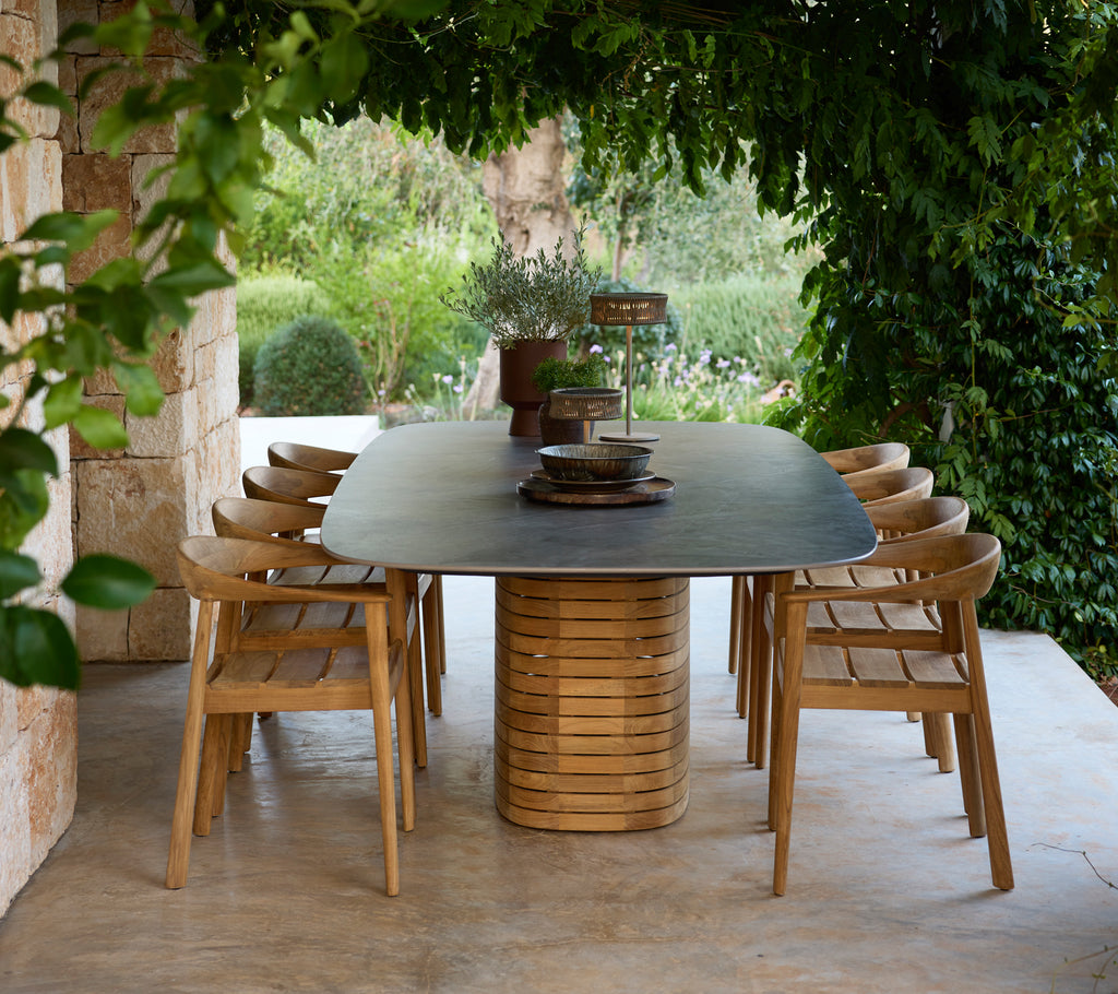 Mesa de comedor moderna al aire libre con sillas de madera rodeadas de vegetación.