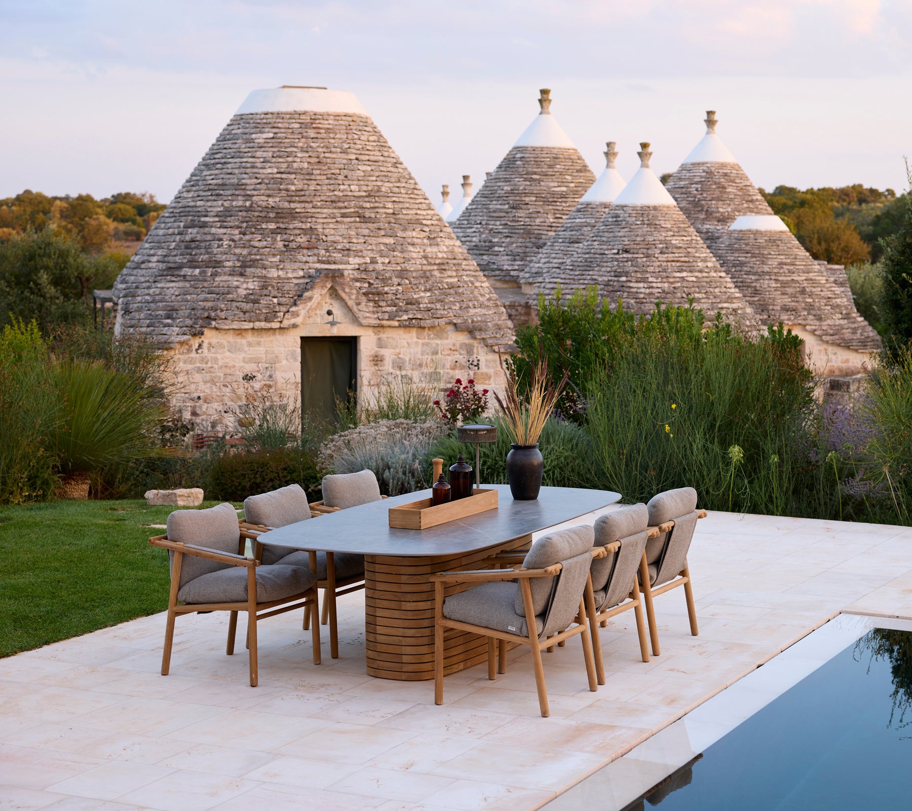 Sillas de comedor grises alrededor de una mesa rectangular cerca de estructuras trullo tradicionales.