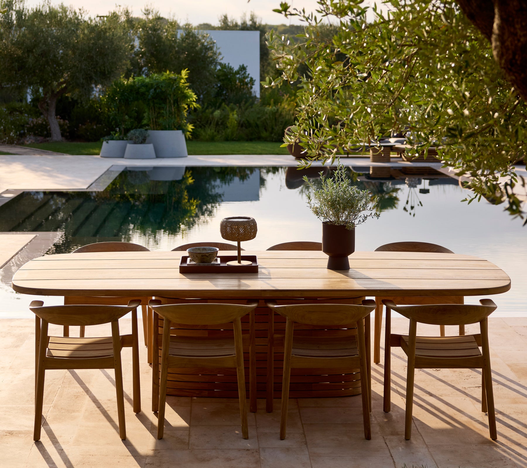 Conjunto de mesa y sillas de madera modernas cerca de una piscina rodeada de vegetación.