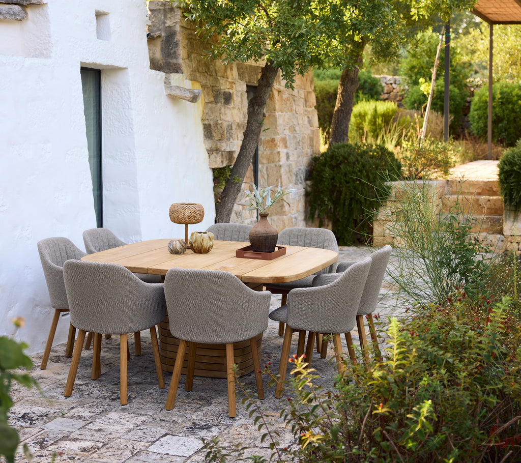 Mesa de comedor de madera moderna rodeada de sillas grises en un entorno de jardín.
