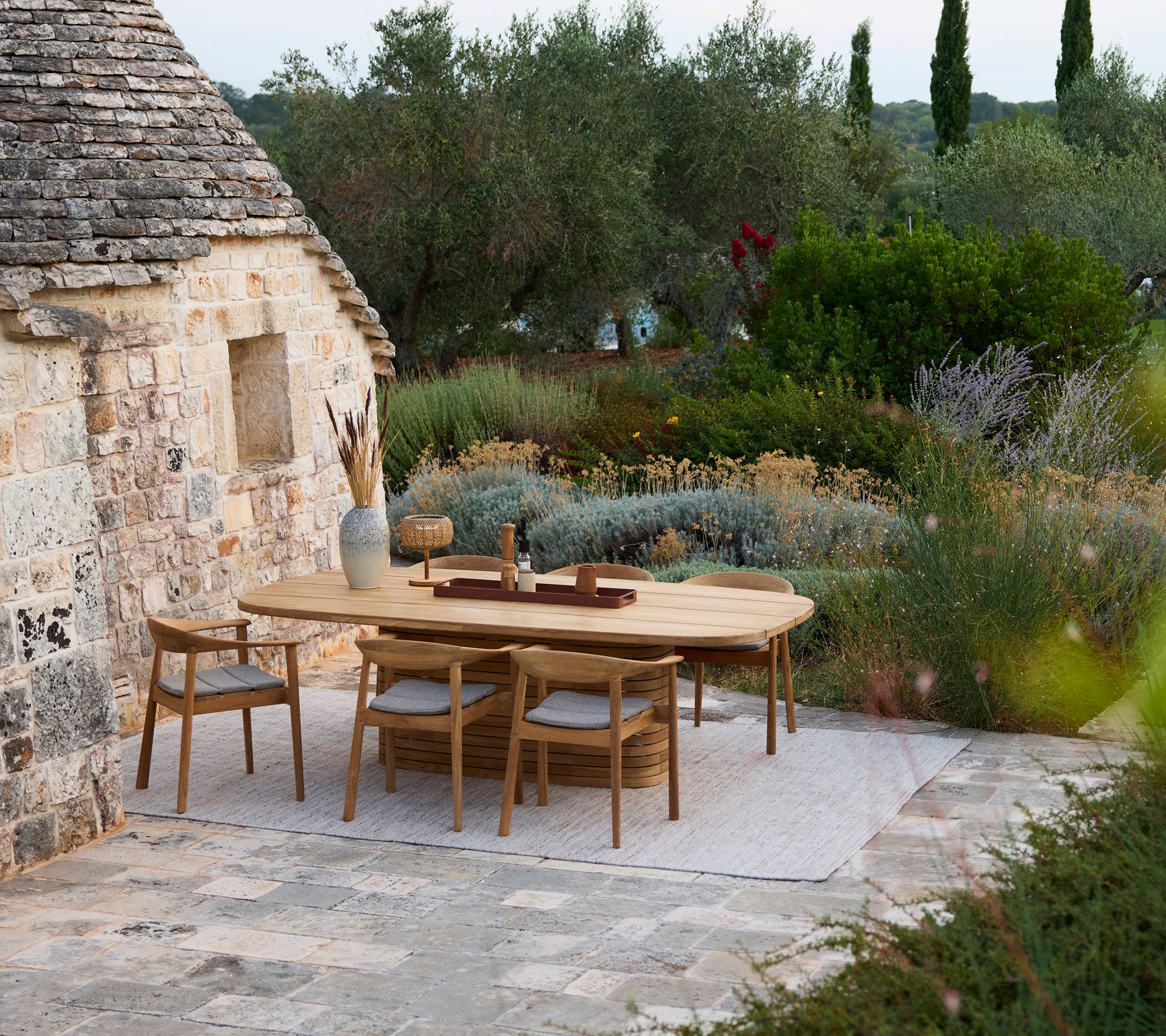 Mesa de comedor de madera moderna rodeada de sillas de madera en un entorno de jardín al aire libre.