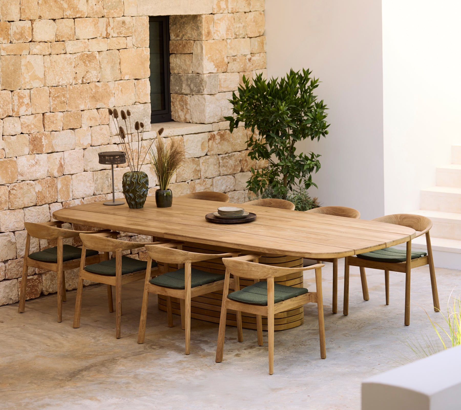 Mesa de comedor de madera moderna con cojines verdes y sillas de madera en un entorno minimalista.