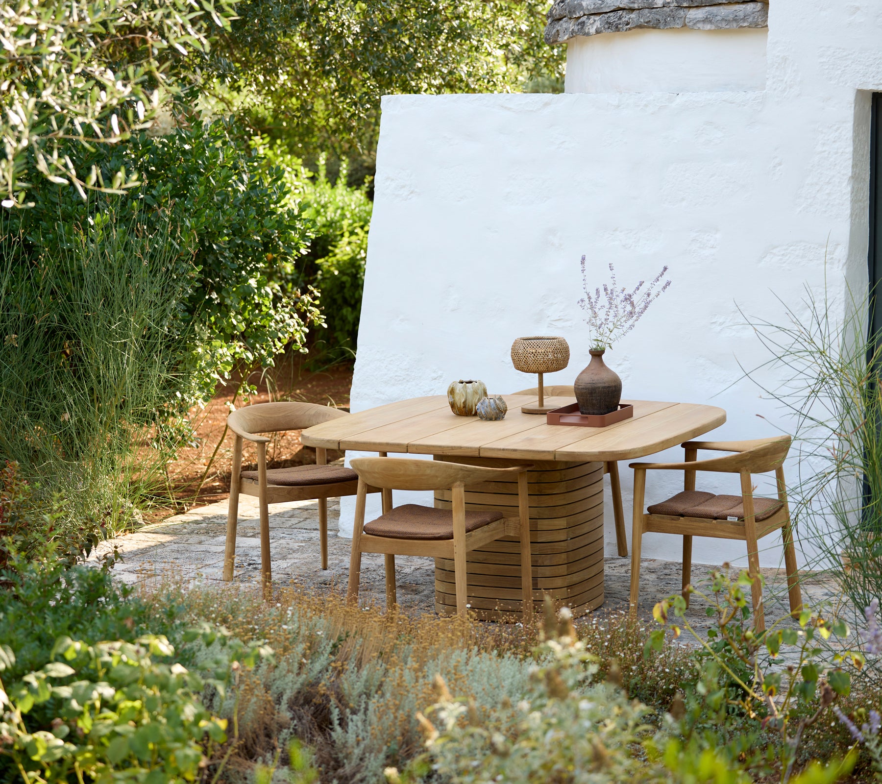 Mesa redonda moderna con sillas de madera y un jarrón decorativo en un entorno al aire libre.