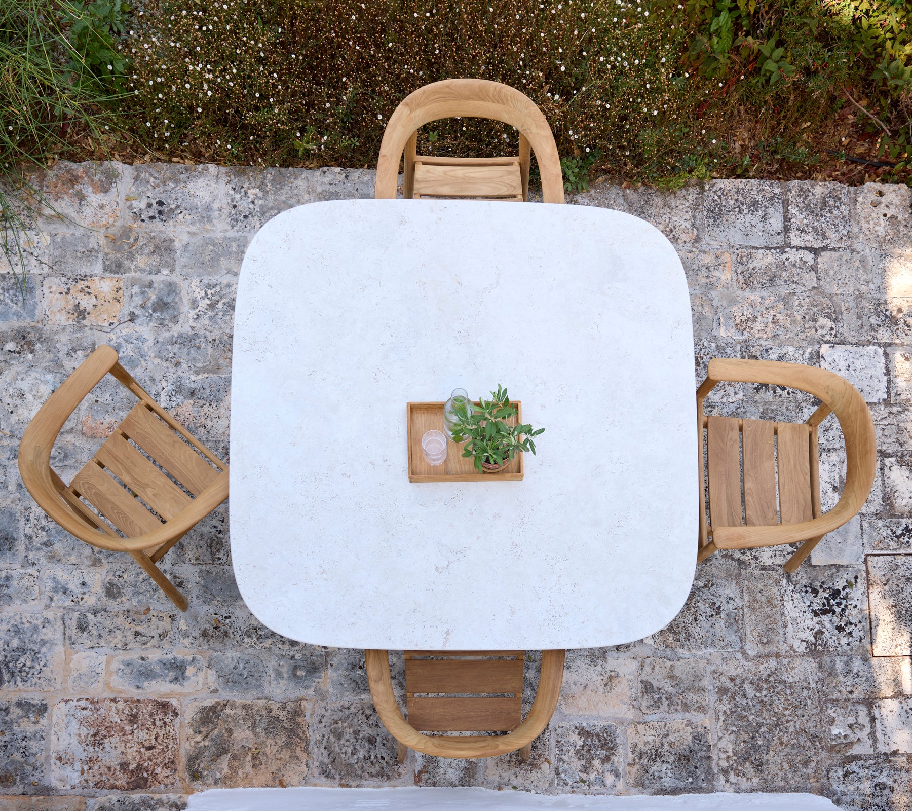 Mesa blanca moderna con sillas de madera y un pequeño centro de planta en un entorno al aire libre.