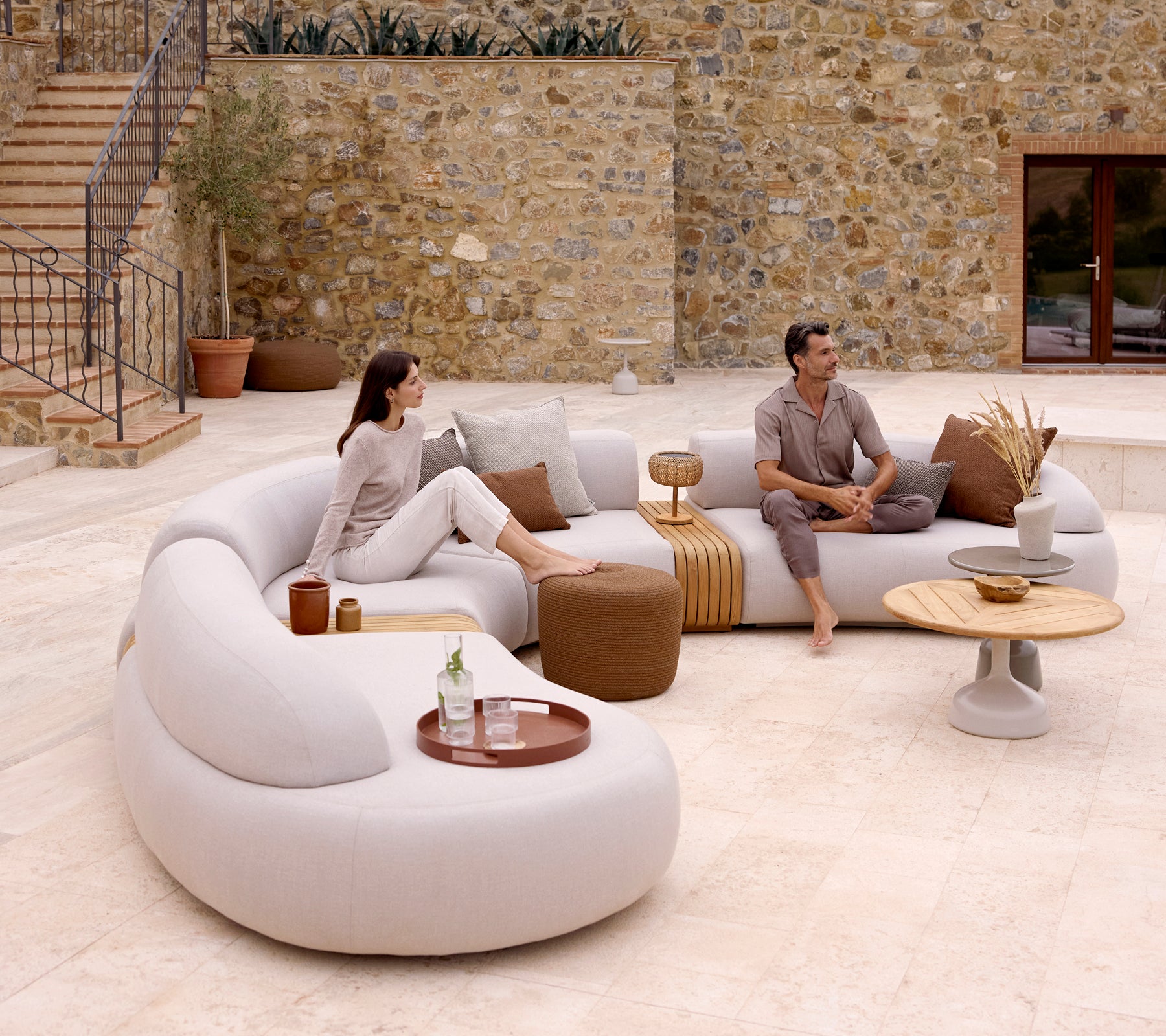Una configuración de salón moderna con un sofá curvado, un taburete redondo y una mesa de café elegante con una bandeja de club, creando una atmósfera acogedora.