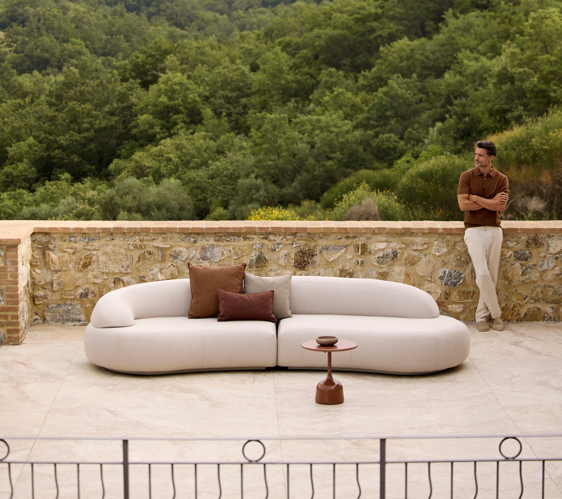 Sofá lounge Mellow con cojines Rise y una mesa de café Glaze, situado frente a un exuberante fondo verde.