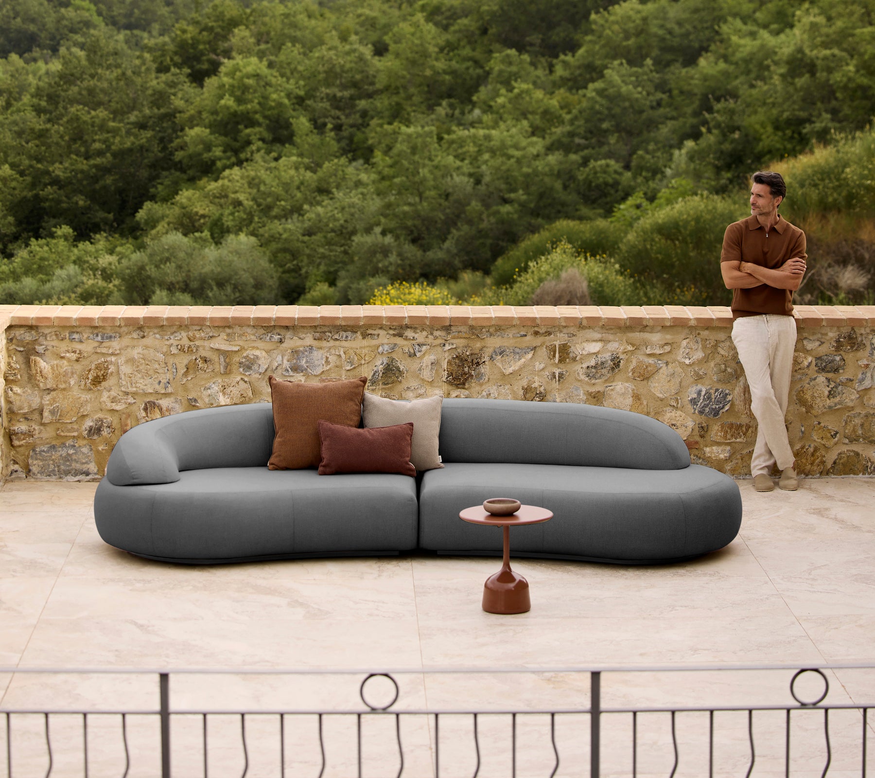 Sofá lounge Mellow con cojines al lado de una elegante mesa de café Glaze, ambientado en un fondo natural.