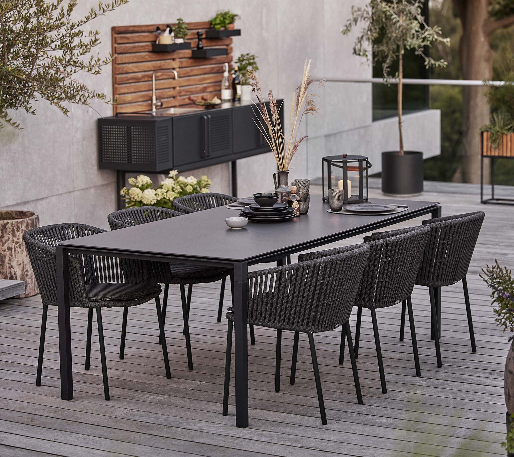 Una mesa negra elegante con seis sillas Moments, con vajilla y elementos decorativos para una experiencia culinaria acogedora.