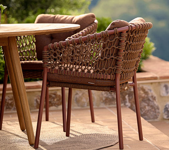 Una silla roja elegante con detalles trenzados al lado de una mesa de comedor de madera, complementando un ambiente exterior relajado.