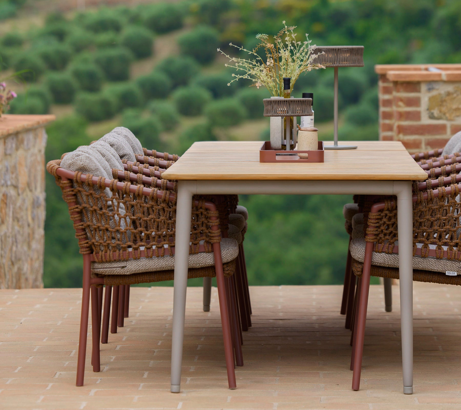 Sillas de comedor color marrón umber rodeando una mesa elegante, acentuadas con una bandeja de club y elementos decorativos, contra un fondo escénico.