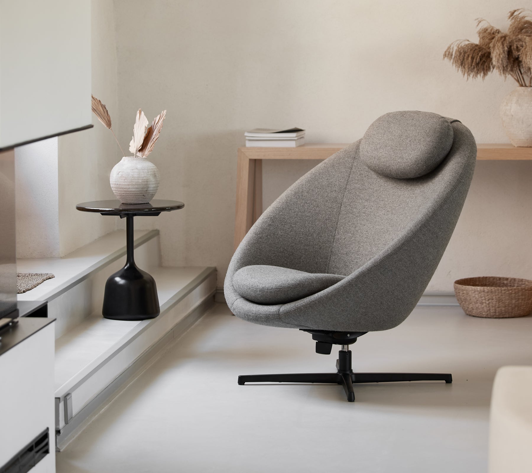 Silla gris elegante con forma curva y reposacabezas, complementada por una mesa auxiliar minimalista y elementos decorativos.