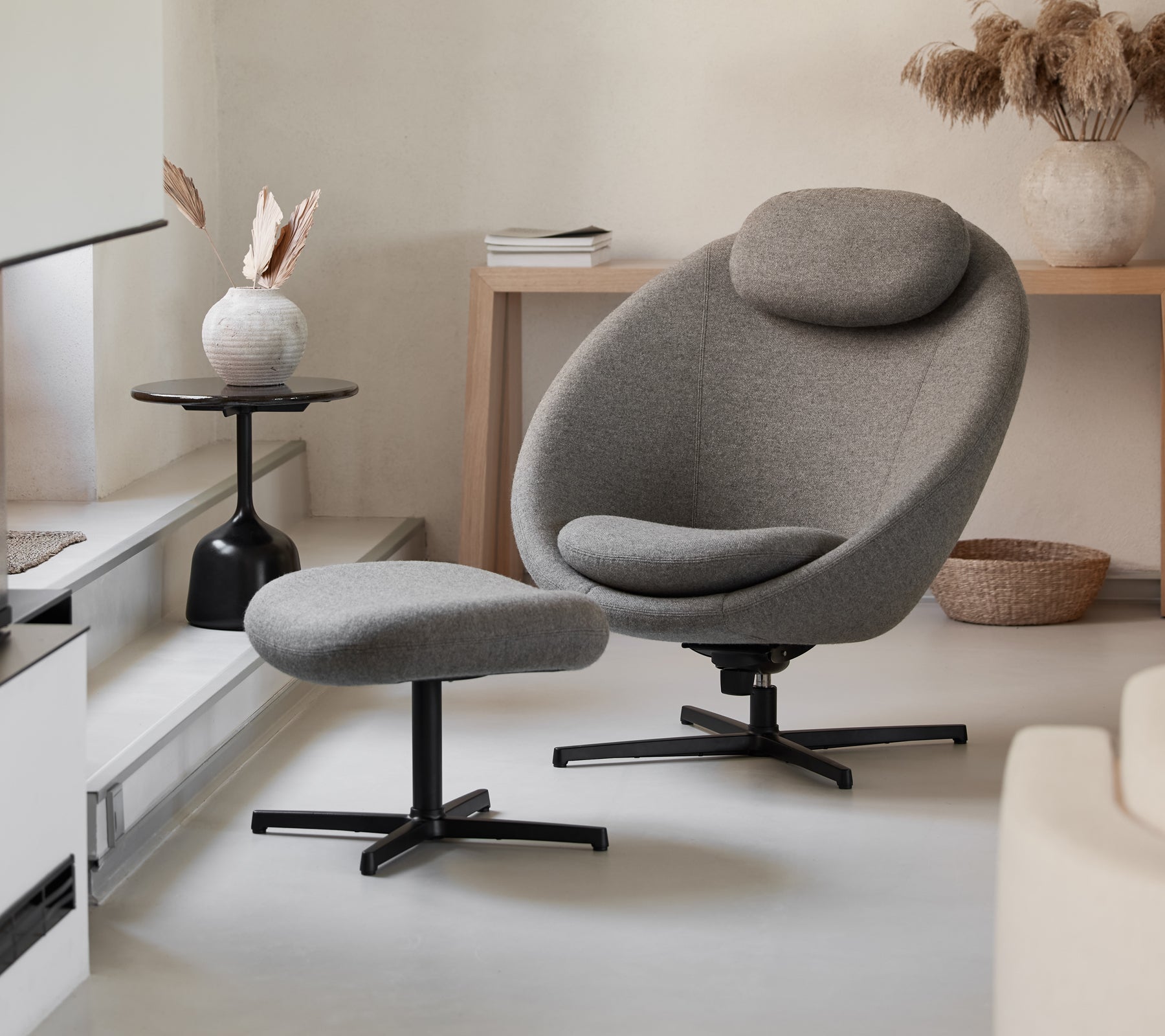 Silla gris elegante con otomana a juego, que presenta un diseño estilizado y curvas cómodas, complementada con elementos de decoración modernos.