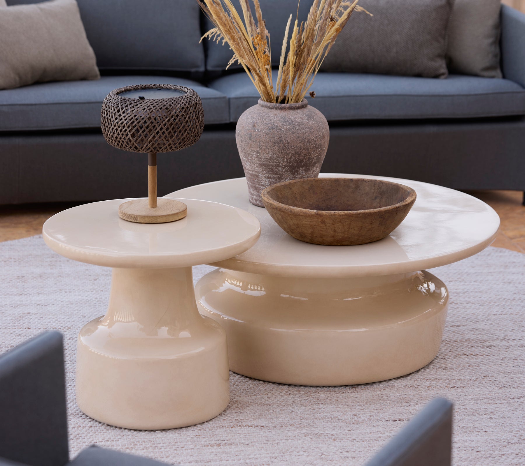 Mesas de café y mesas auxiliares beige modernas con un tazón marrón y una lámpara de metal en un ambiente de salón.