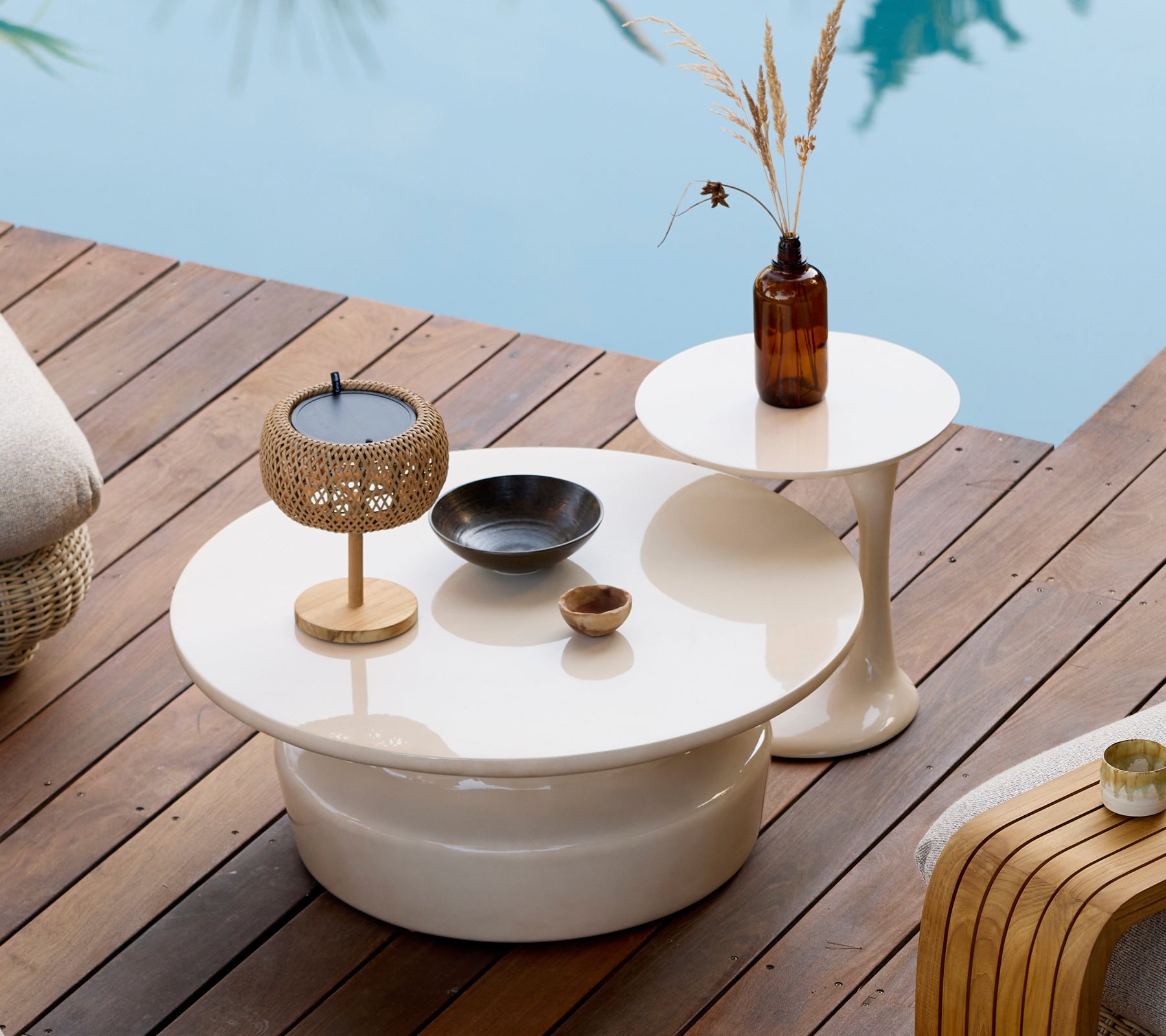 Configuración moderna al aire libre con mesas de café y mesas auxiliares blancas, portavelas dorado y jarrón marrón.