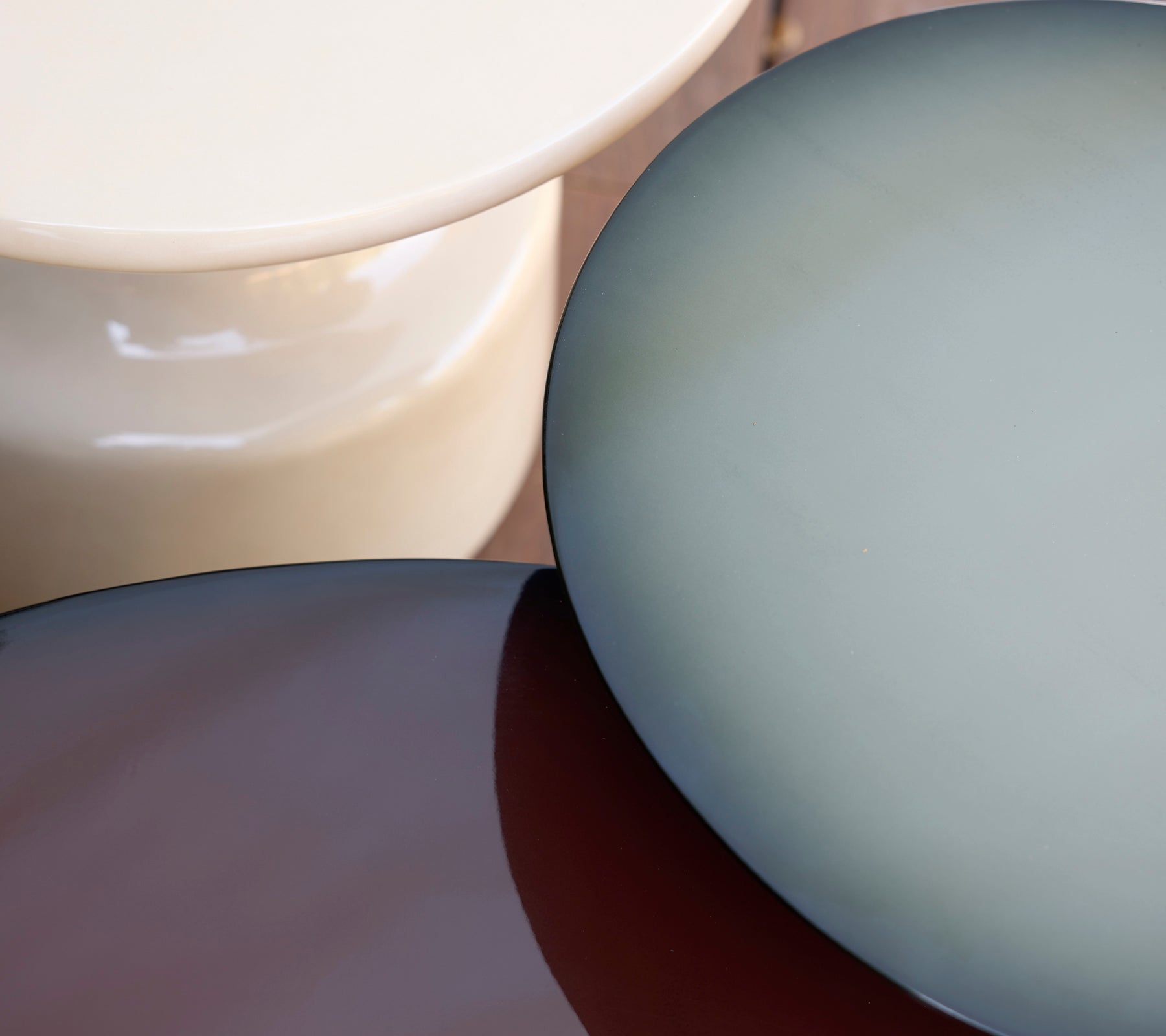 Tres mesas modernas en tonos crema, azul y marrón dispuestas juntas.