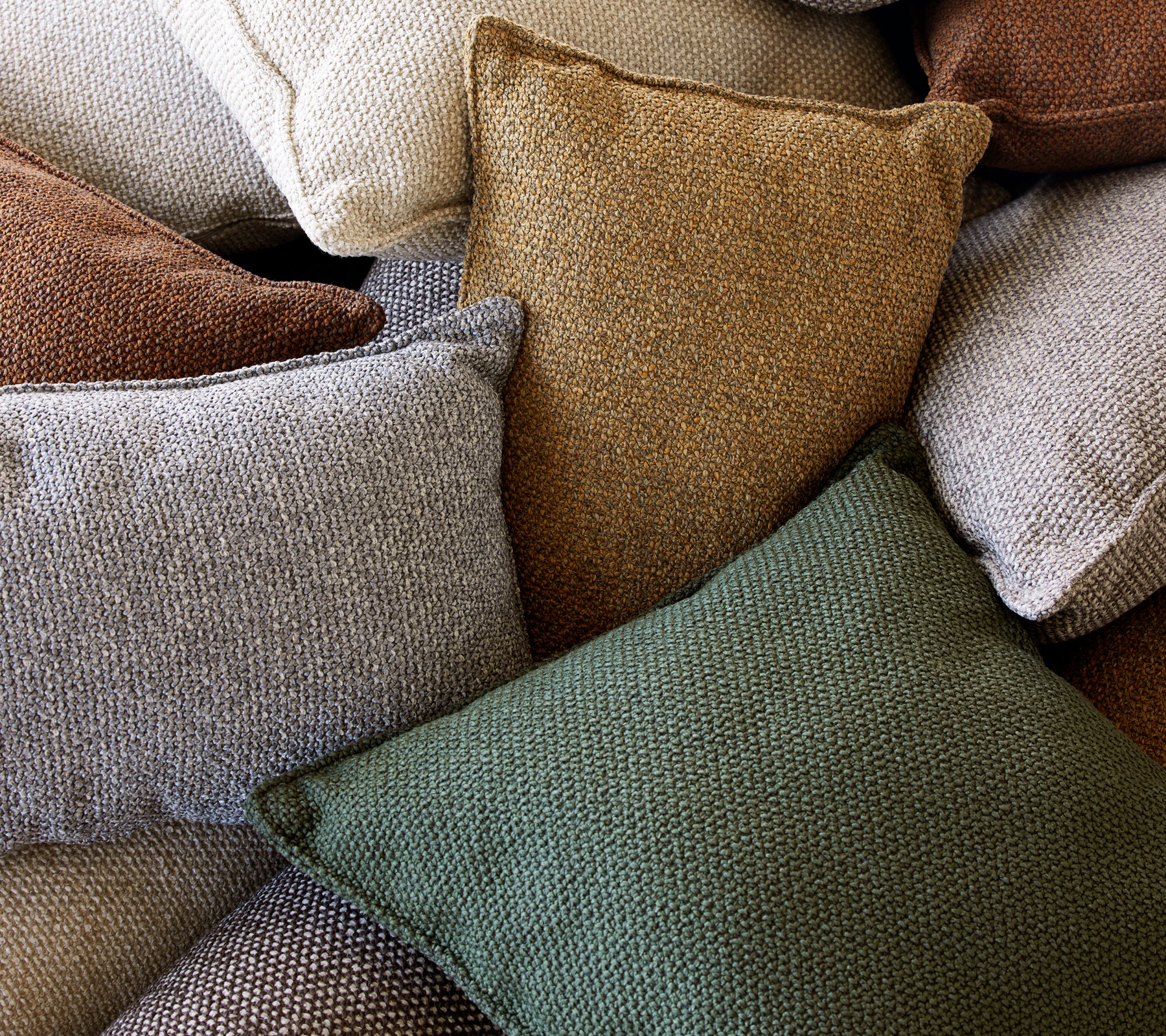 Una colección de cojines texturizados en varios colores, incluyendo verde, marrón y crema, apilados juntos.