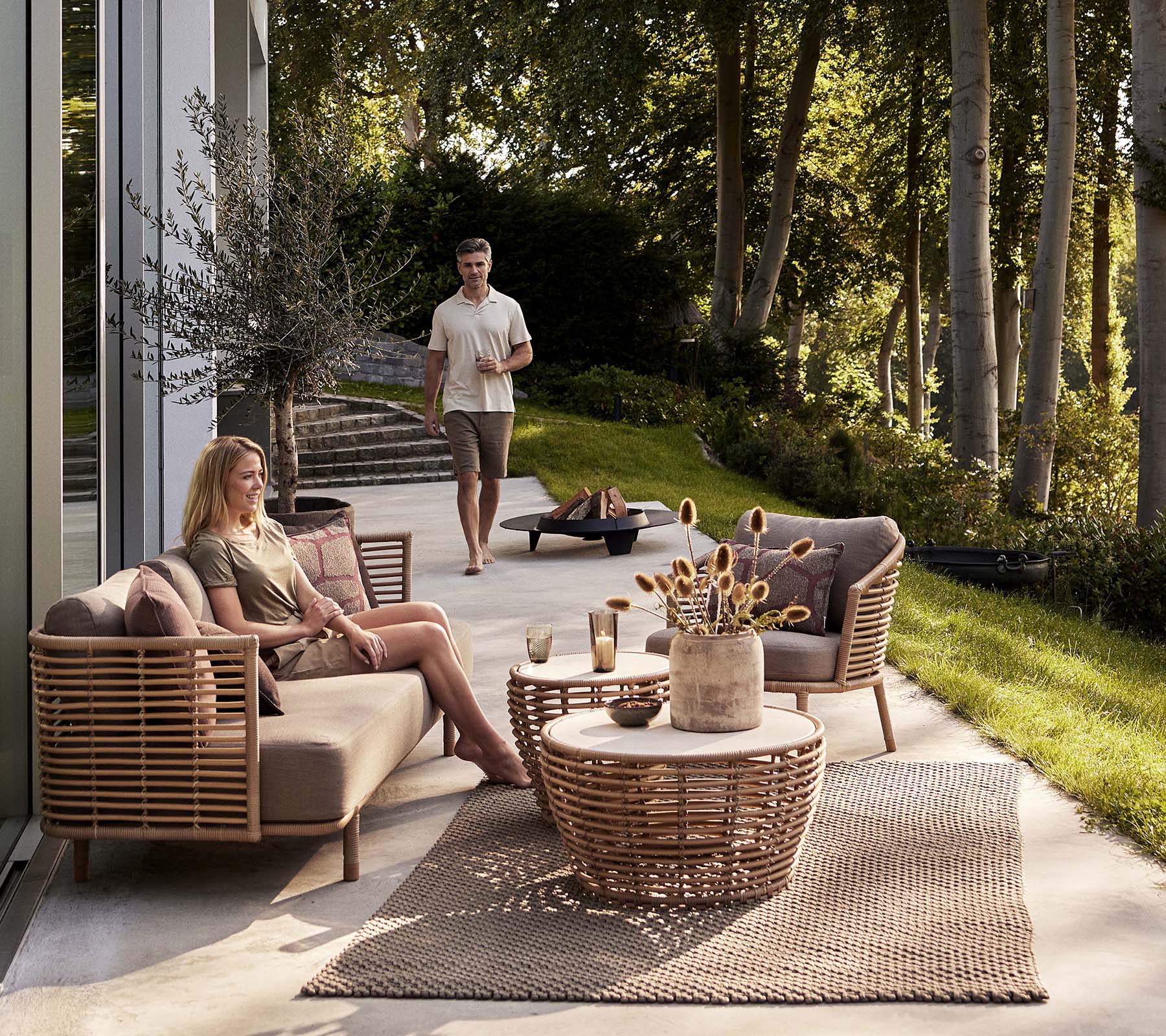 Un acogedor arreglo de asientos con un sofá Sense y una silla lounge, acompañado de una mesa de café de mimbre y elementos decorativos.