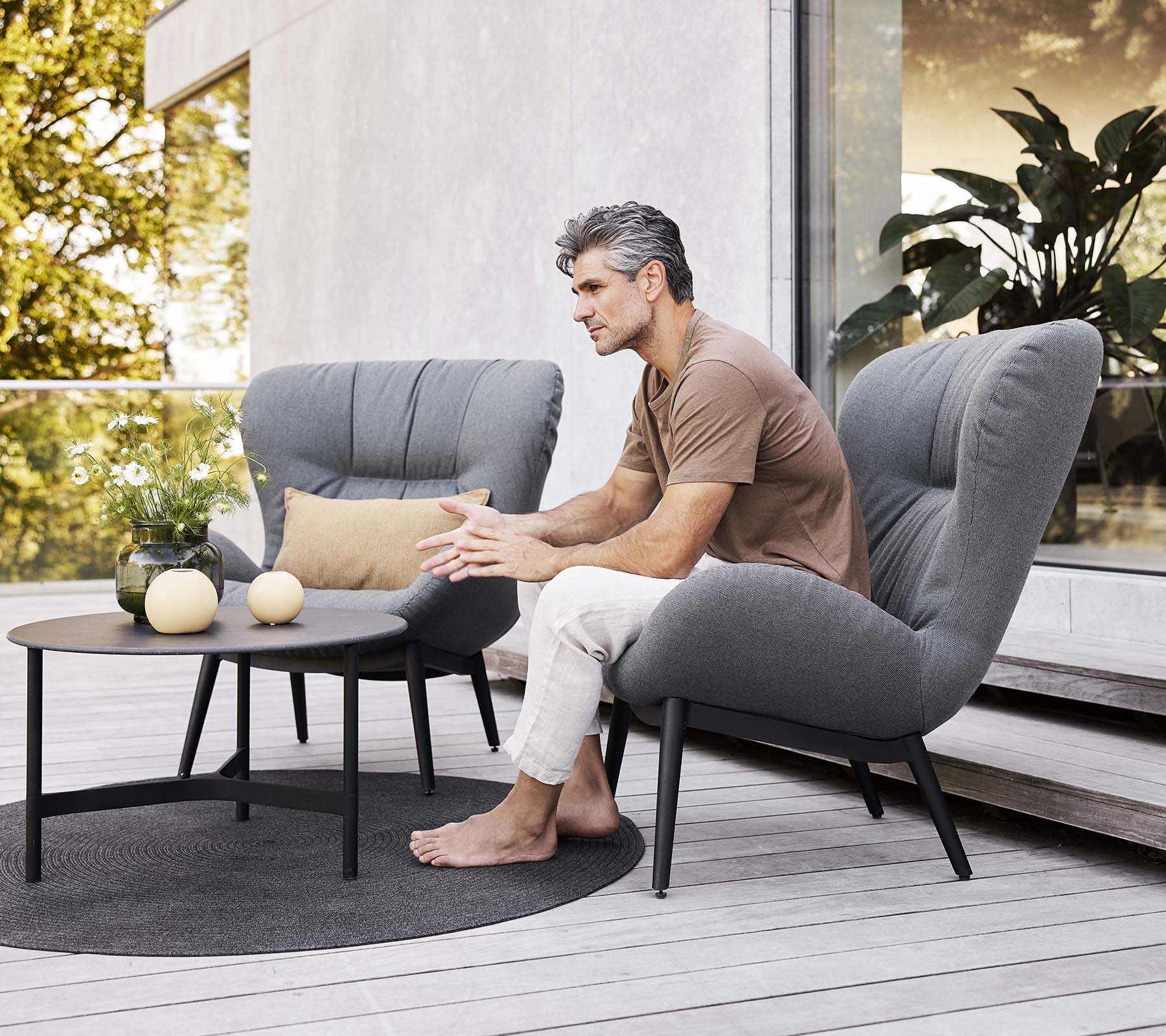 Una silla de salón serena con un hombre sentado, una pequeña mesa cerca y elementos decorativos, creando una atmósfera relajada.