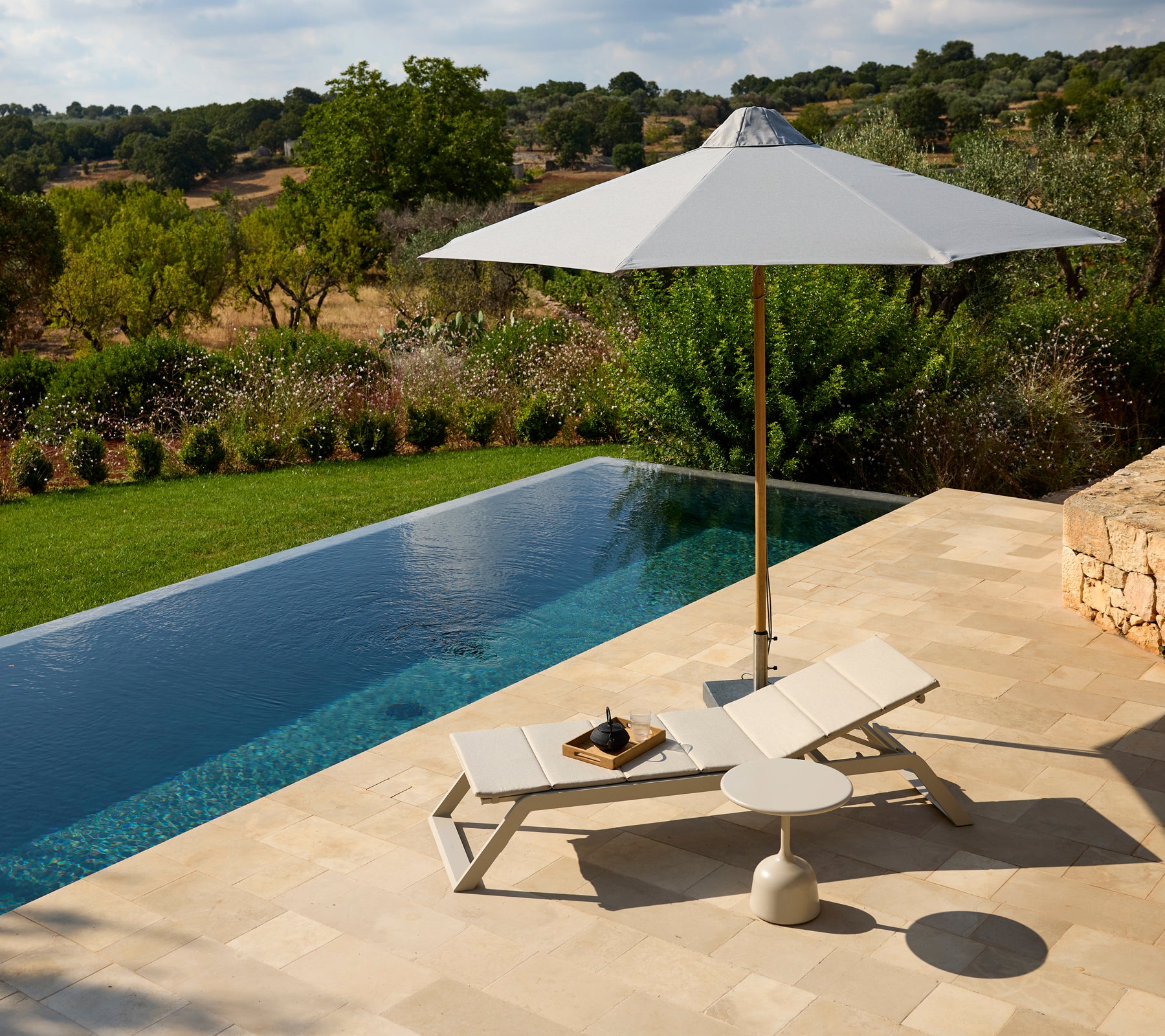 Moderna área de salón al aire libre con una silla blanca, una sombrilla y una mesa auxiliar junto a una piscina.
